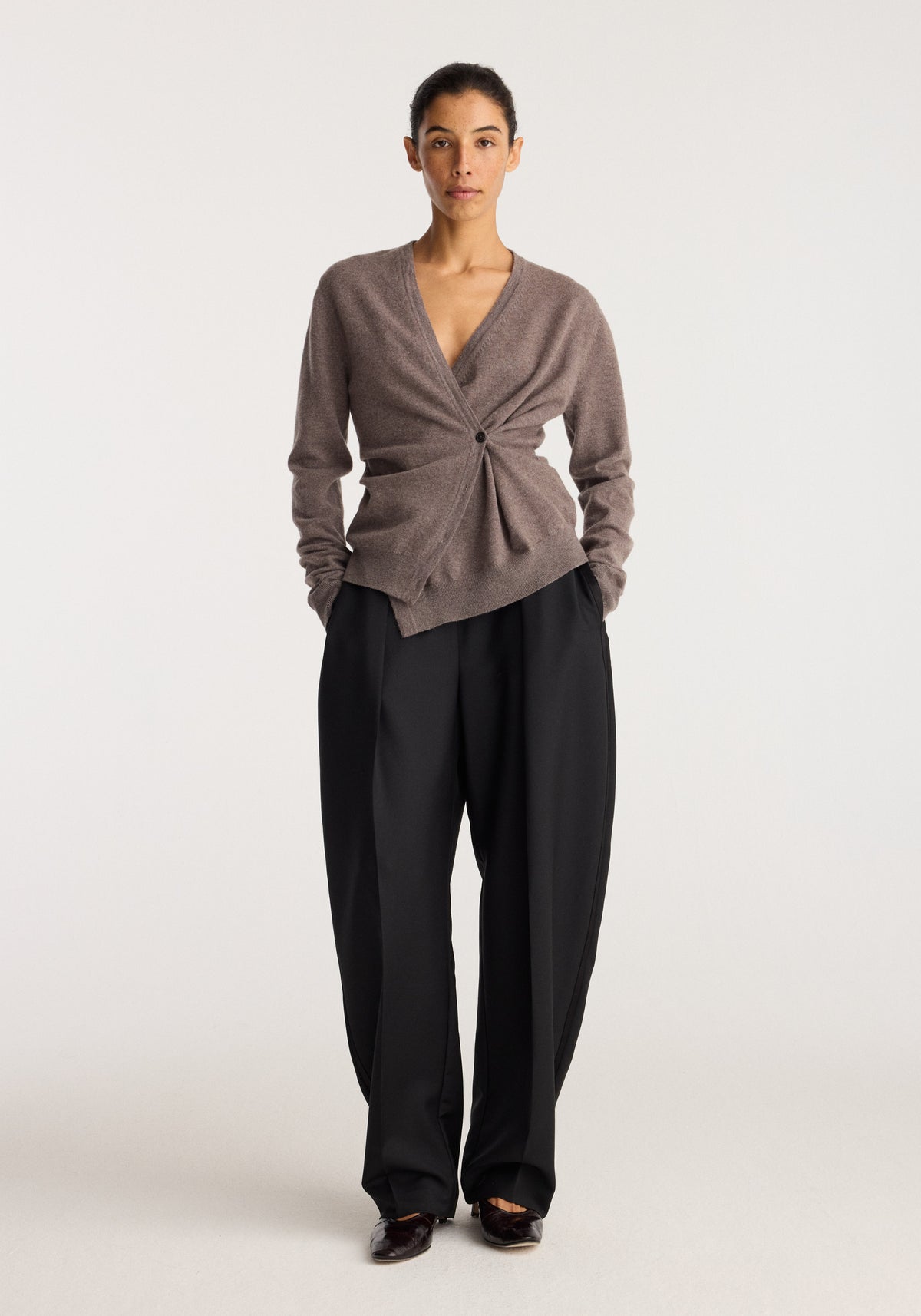 Twisted ballet cardigan | mud modeled on a woman with a twisted front, long sleeves, deep V neckline, and relaxed black trousers in a studio setting