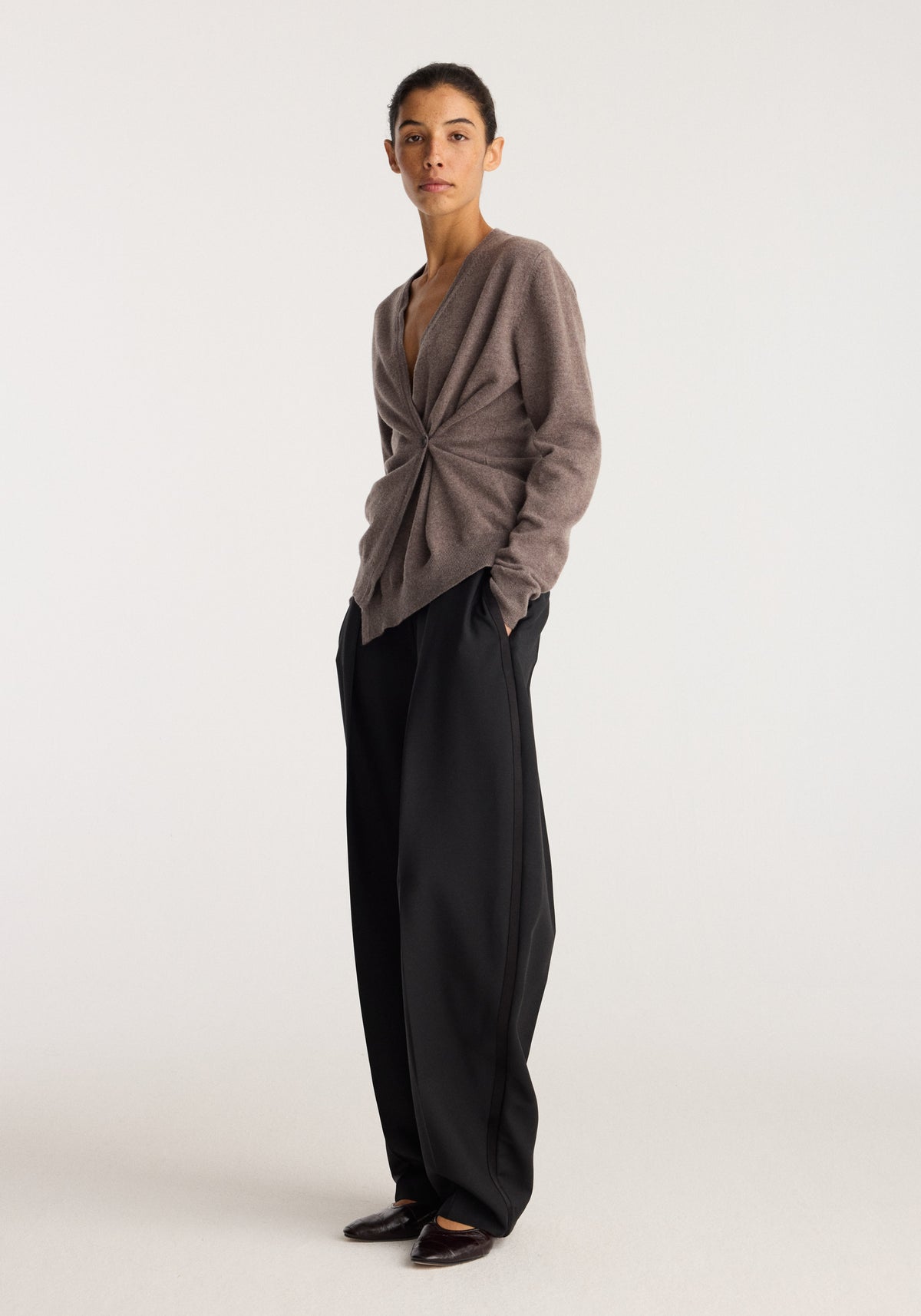 Twisted ballet cardigan | mud in brown worn by a model with a twisted front and relaxed fit, styled with black wide leg trousers and flats