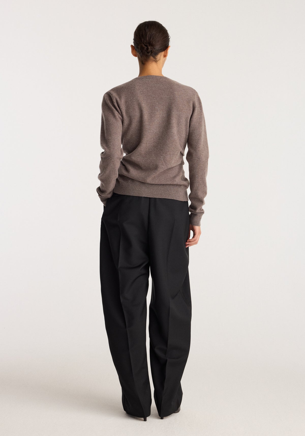 Twisted ballet cardigan | mud shown from the back on a model with black trousers in a minimal studio setting