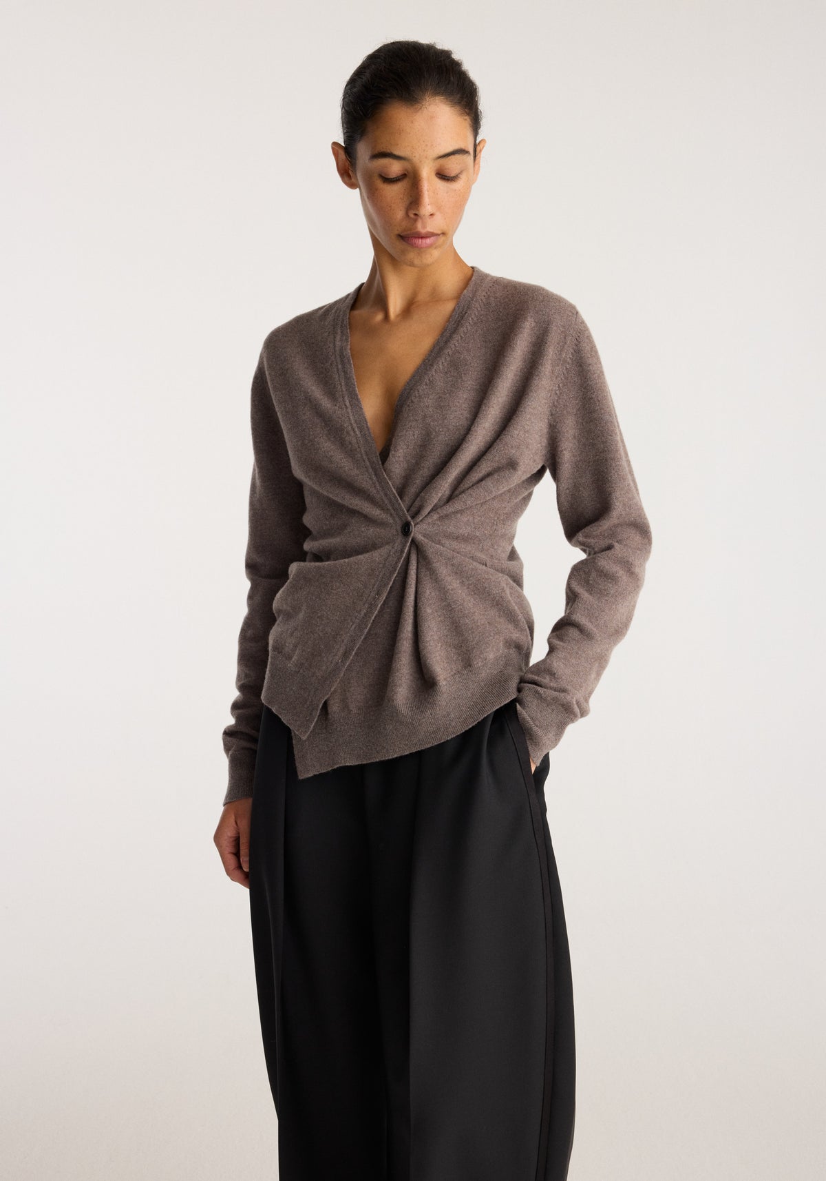 Model wearing Twisted ballet cardigan | mud in a soft brown shade with a twisted front detail and long sleeves paired with black trousers