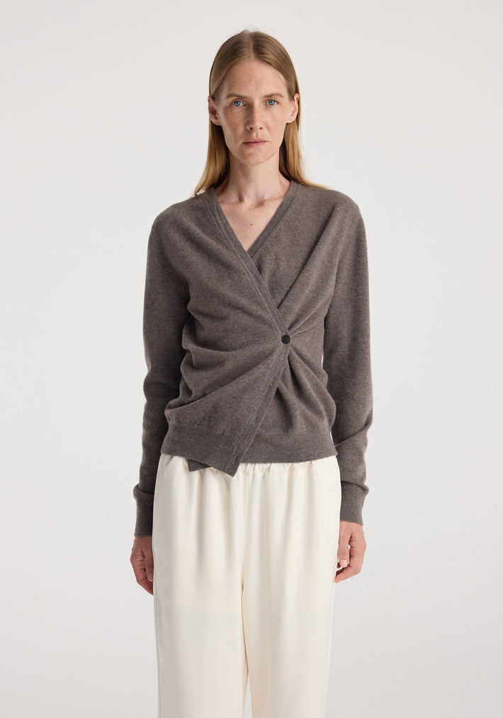 Woman wearing a twisted design wrap cardigan in a muted brown shade paired with loose white pants, styled simply against a plain background, showcasing the Twisted ballet cardigan | mud.
