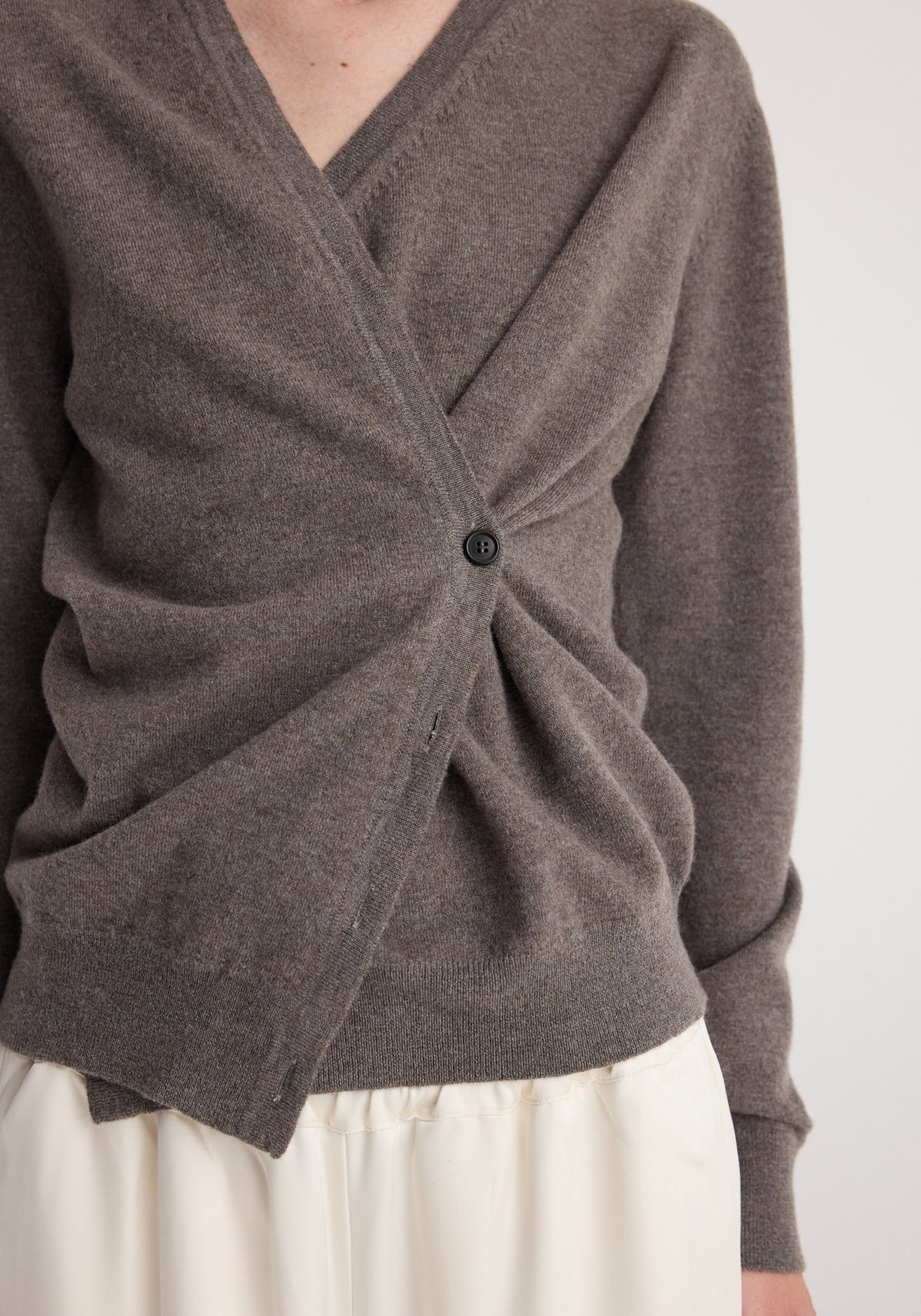 Close-up of a person wearing a soft, mud-colored twisted ballet cardigan | mud with a single button fastening and a ruched detail at the front, paired with a light-colored skirt.