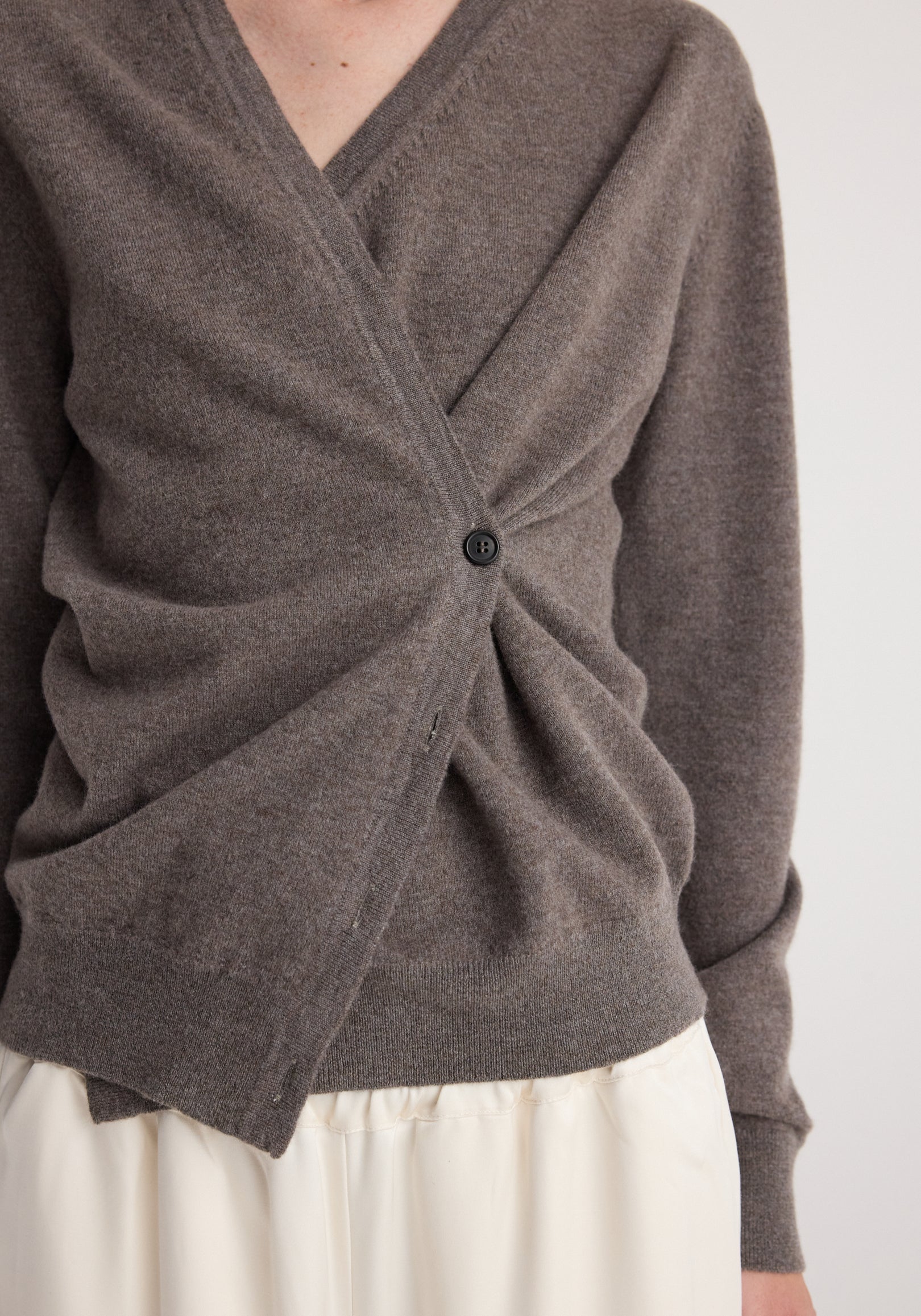 Close-up of a person wearing a soft, mud-colored twisted ballet cardigan | mud with a single button fastening and a ruched detail at the front, paired with a light-colored skirt.
