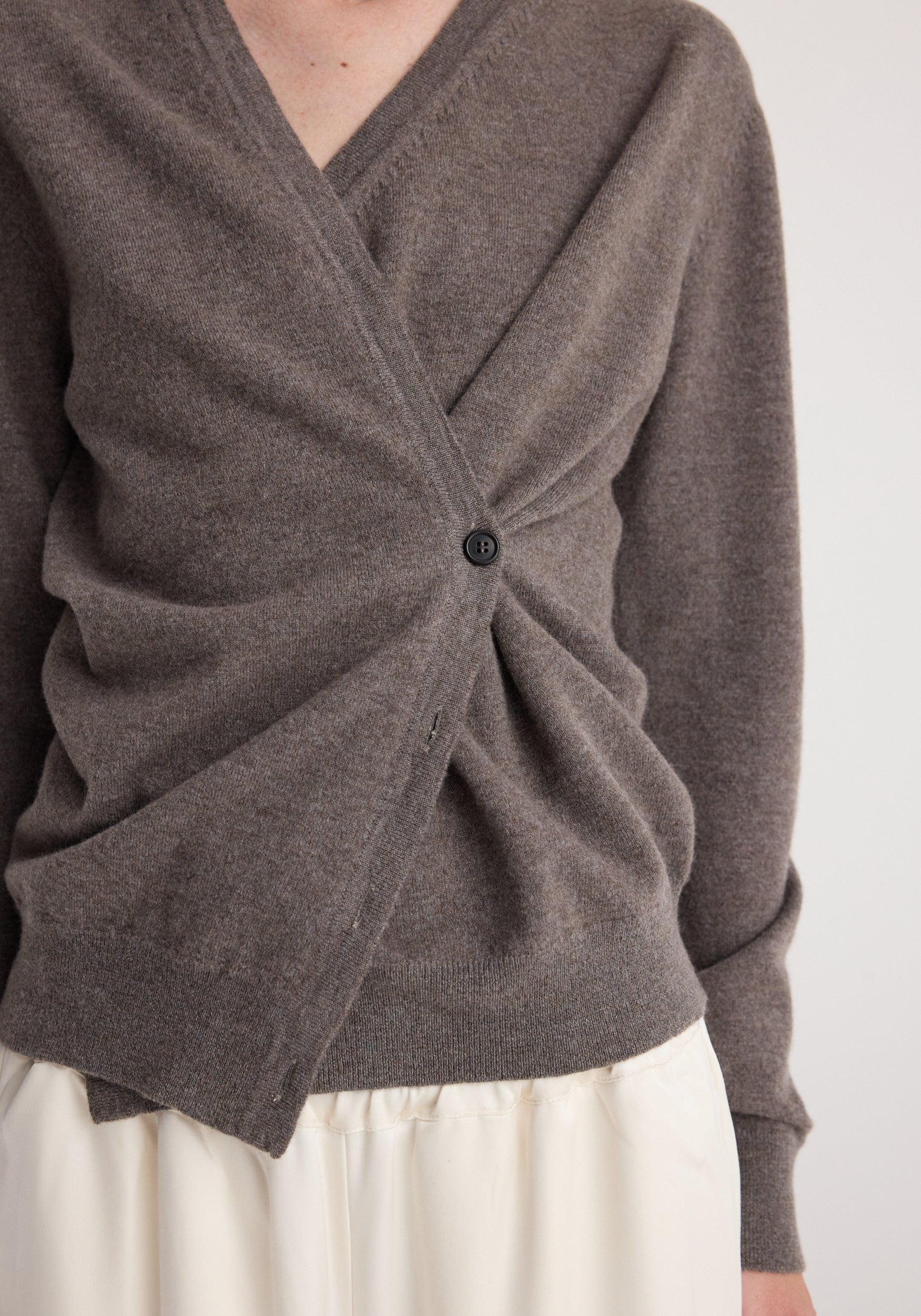 Close-up of a person wearing a soft, mud-colored twisted ballet cardigan | mud with a single button fastening and a ruched detail at the front, paired with a light-colored skirt.