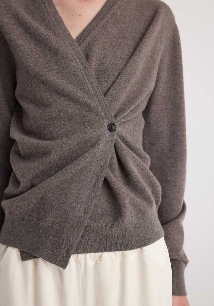 Close-up of a person wearing a soft, mud-colored twisted ballet cardigan | mud with a single button fastening and a ruched detail at the front, paired with a light-colored skirt.