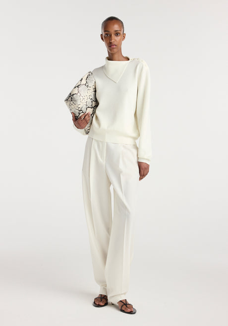 Model wearing an off white uneven collar polo paired with matching wide-leg trousers, holding a snakeskin-patterned clutch bag and wearing black strappy sandals.