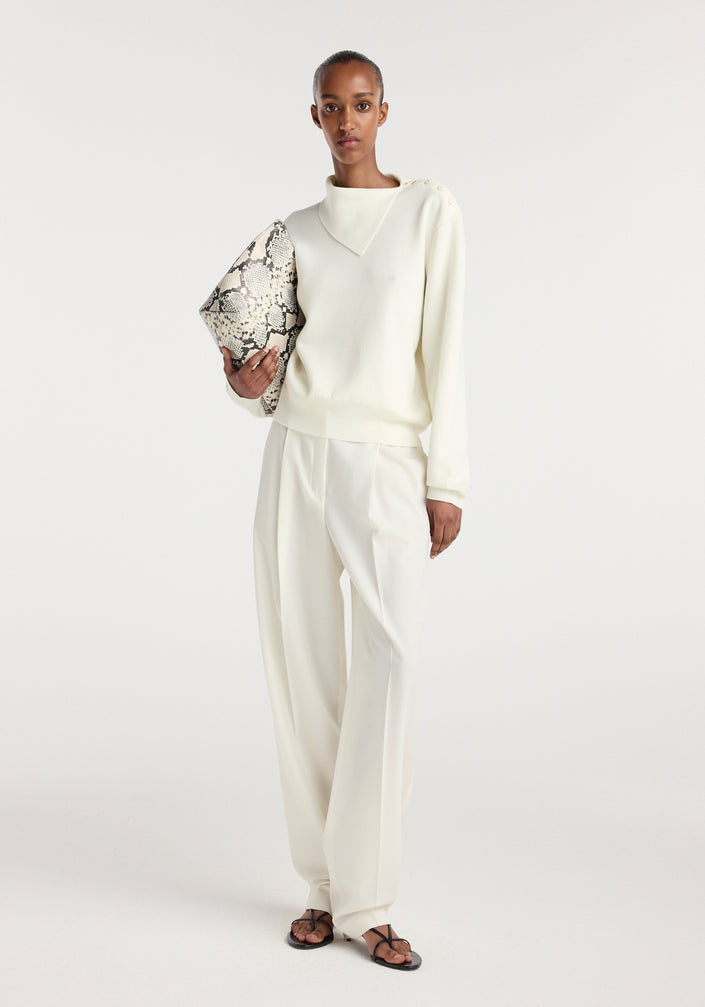 Model wearing an off white uneven collar polo paired with matching wide-leg trousers, holding a snakeskin-patterned clutch bag and wearing black strappy sandals.