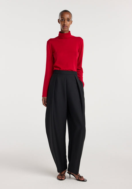 Woman wearing a bright red fine-knit wool cashmere turtleneck paired with high-waisted wide-leg black trousers and black open-toe heeled sandals.