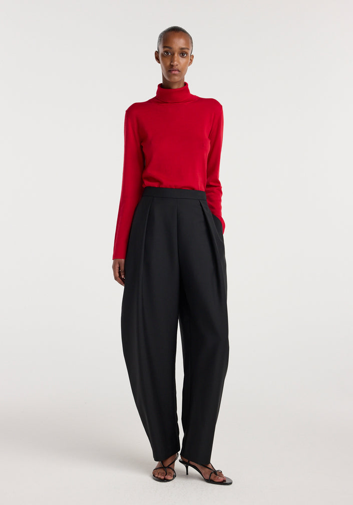 Woman wearing a bright red fine-knit wool cashmere turtleneck paired with high-waisted wide-leg black trousers and black open-toe heeled sandals.