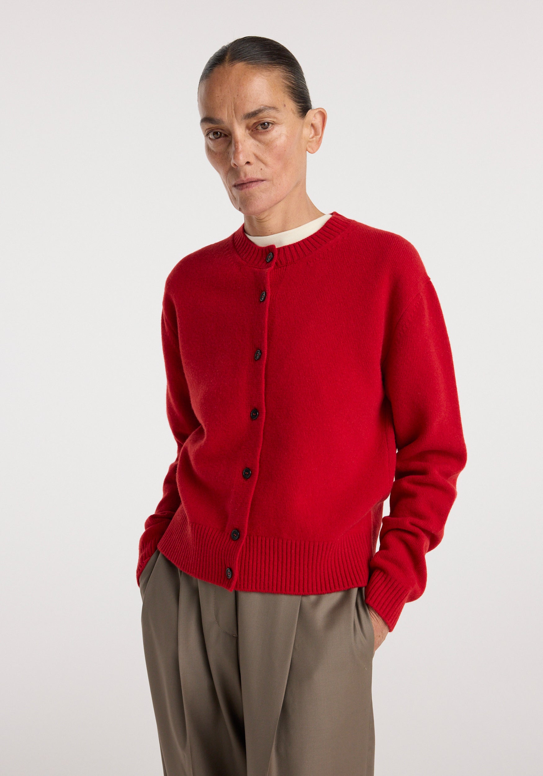 Woman wearing a bright red button-up wool sweater with a round neckline, styled with loose-fitting beige pants, classic cardigan | red.