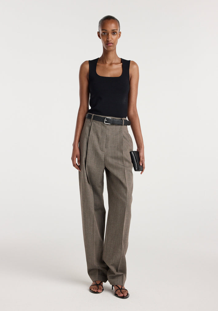 Woman wearing a black sleeveless top paired with Daria - Single pleat tapered trousers | earth slub, featuring a belted waist and straight-leg fit, standing against a plain background.