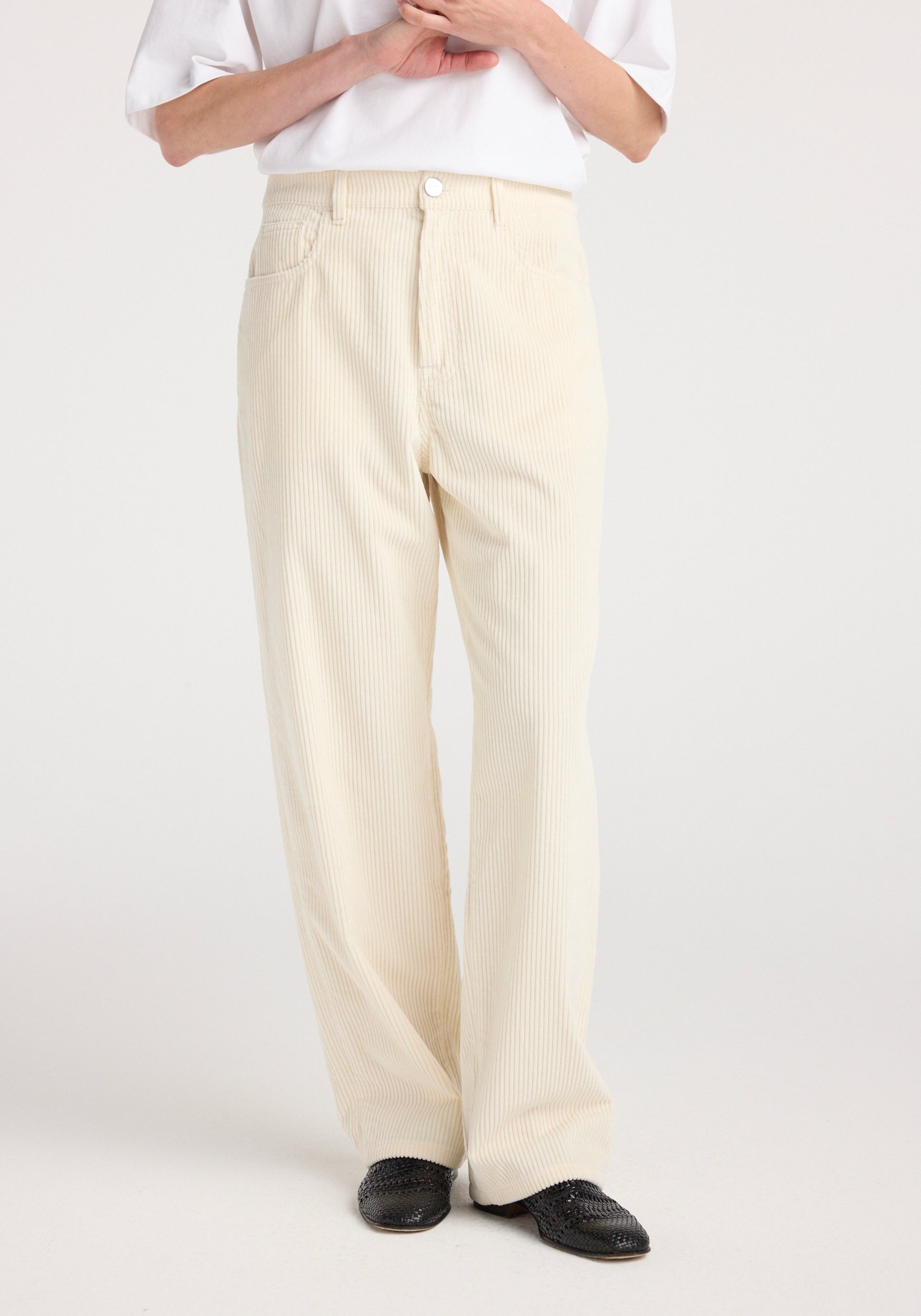Front view of a person wearing winter white Bruun - Signature baggy corduroy pants paired with a white top and black woven shoes, standing against a plain background.
