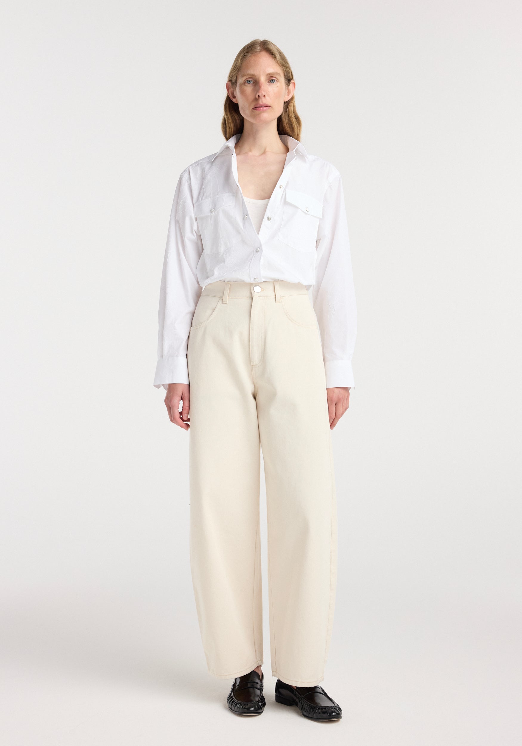 Woman wearing a white button-up shirt paired with beige wide-leg pants, styled with black shoes, showcasing the Berber - Barrel leg denim | ecru.