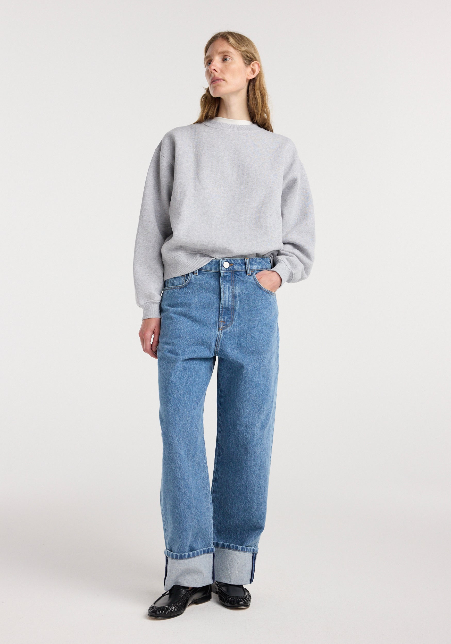 Woman wearing Rixt - Turn-up baggy denim | heritage blue, paired with a grey sweatshirt and black shoes, standing against a plain light background.