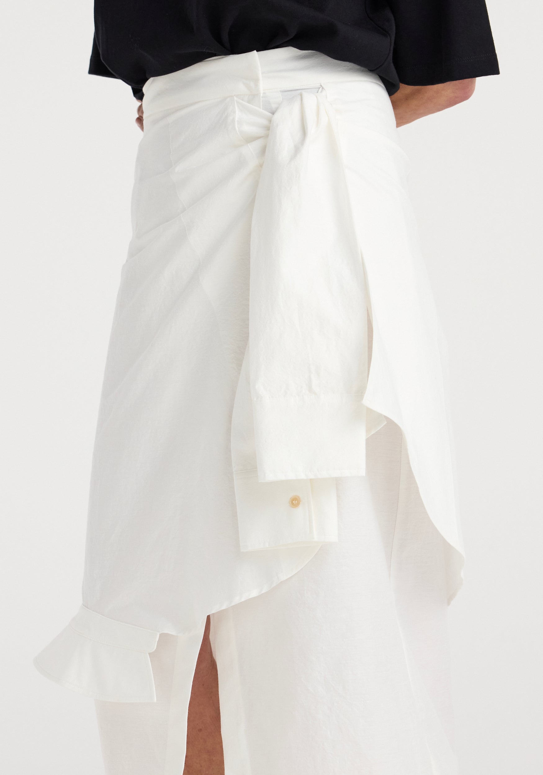 Close-up of a shirt-wrap detailed skirt in optic white, featuring a wraparound design with a tied waist and subtle ruffle accents on lightweight fabric.