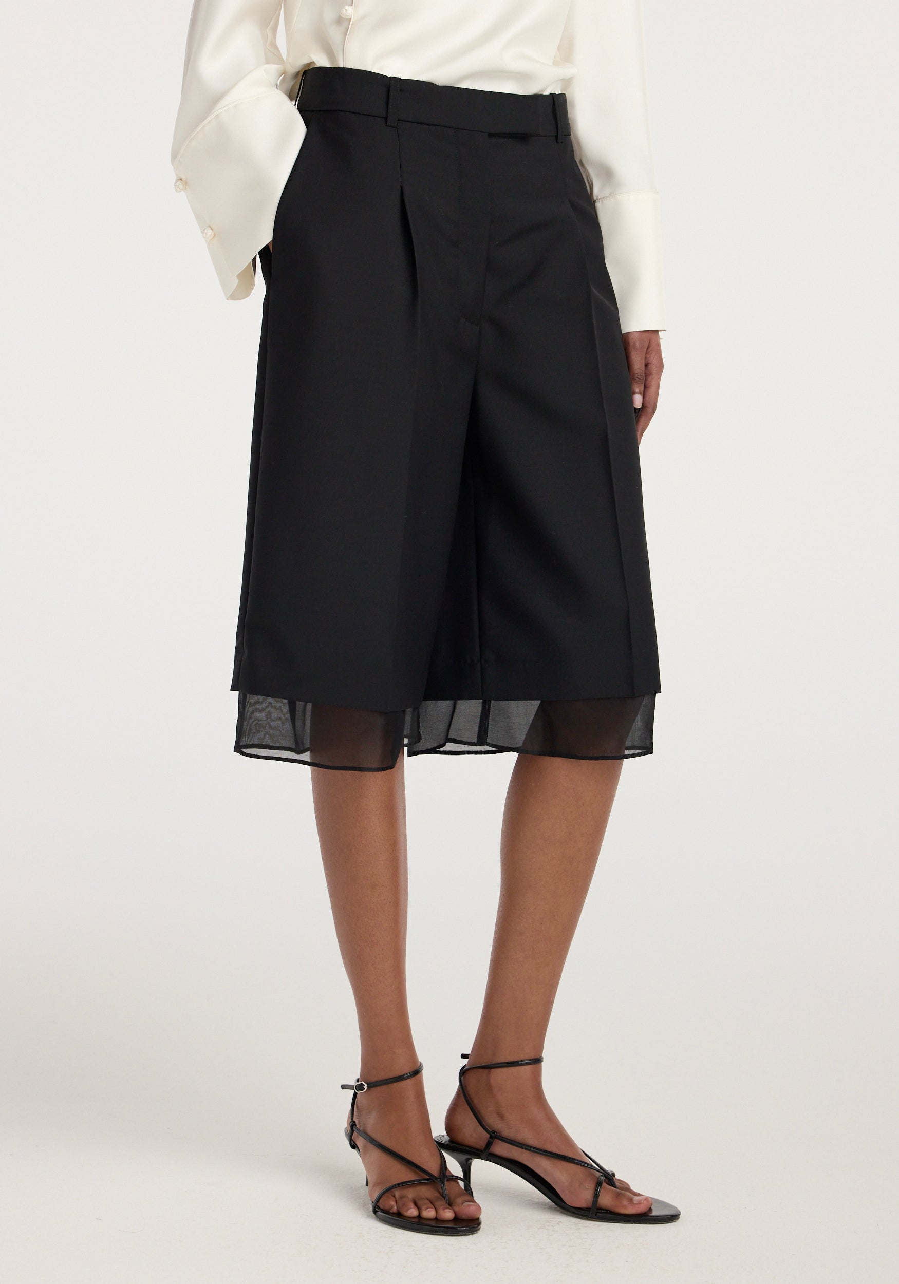 Black organza lined shorts worn by a model paired with black strappy sandals and a white long-sleeve blouse, featuring a tailored fit and knee-length design, Organza lined shorts | black.