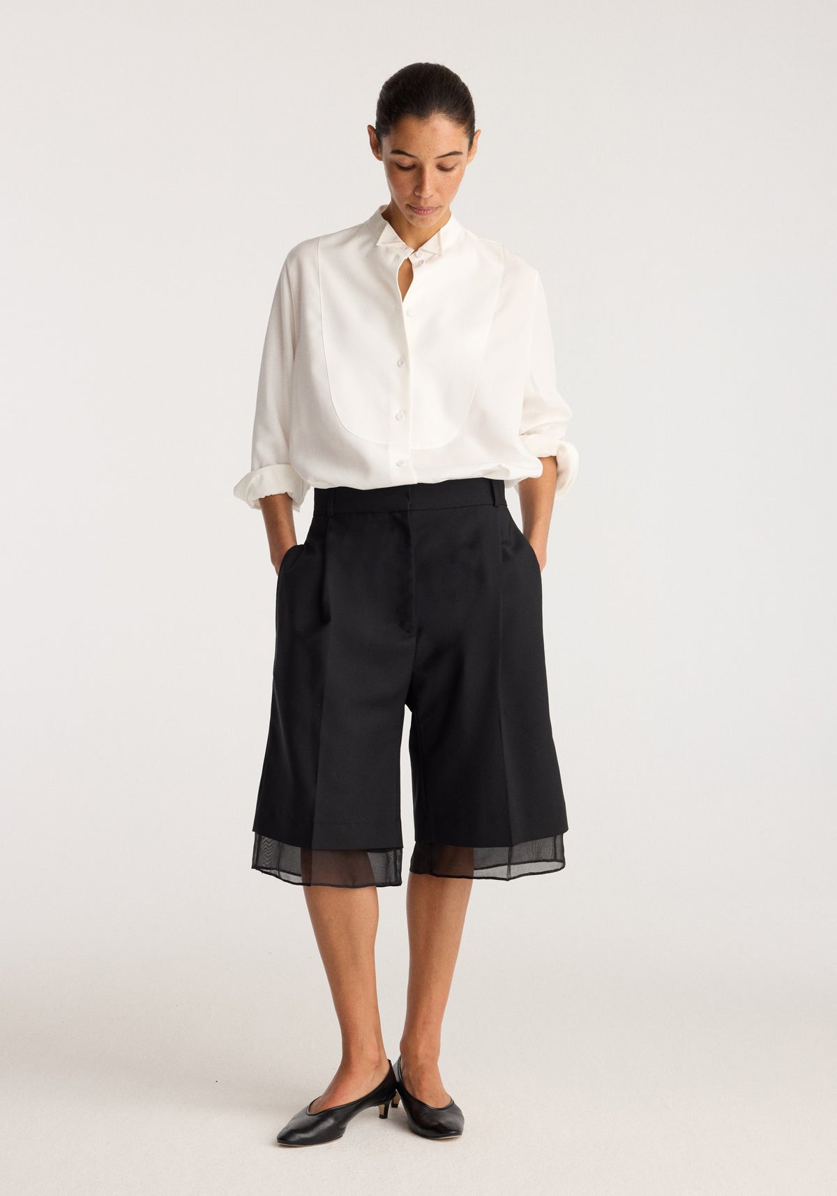 Model wearing Organza lined shorts | black with sheer organza trim at the hem, paired with a white button up shirt and black flats