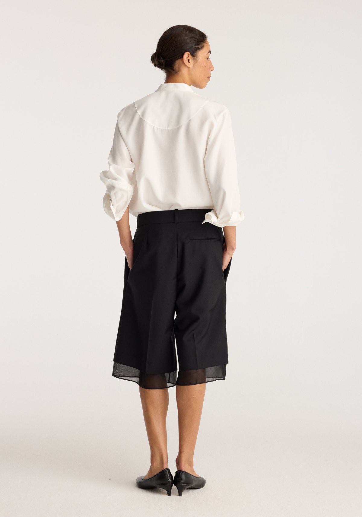 Organza lined shorts | black shown from the back on a model, featuring a relaxed fit, sheer organza hem panels, side pockets, and a high waist.