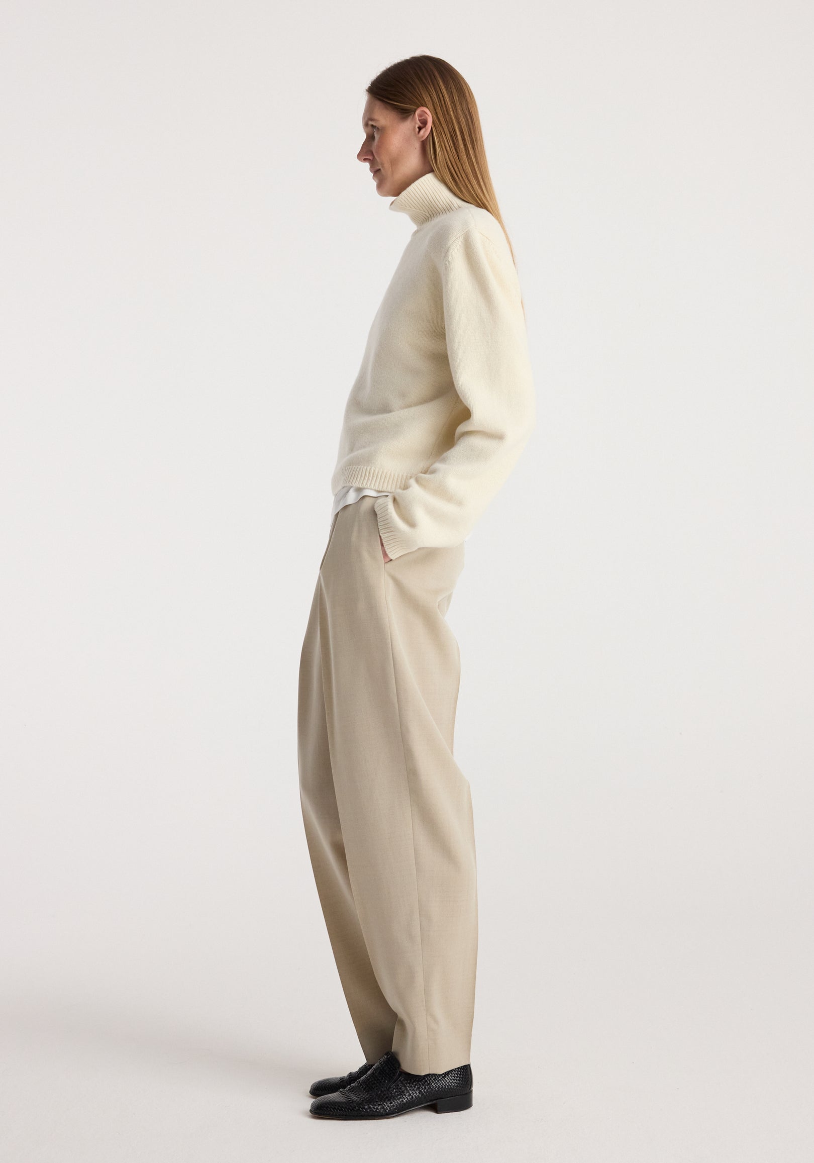 Woman wearing cream Statement shoulder cropped turtleneck | cream paired with beige wide-leg trousers and black shoes, standing sideways against a plain background.