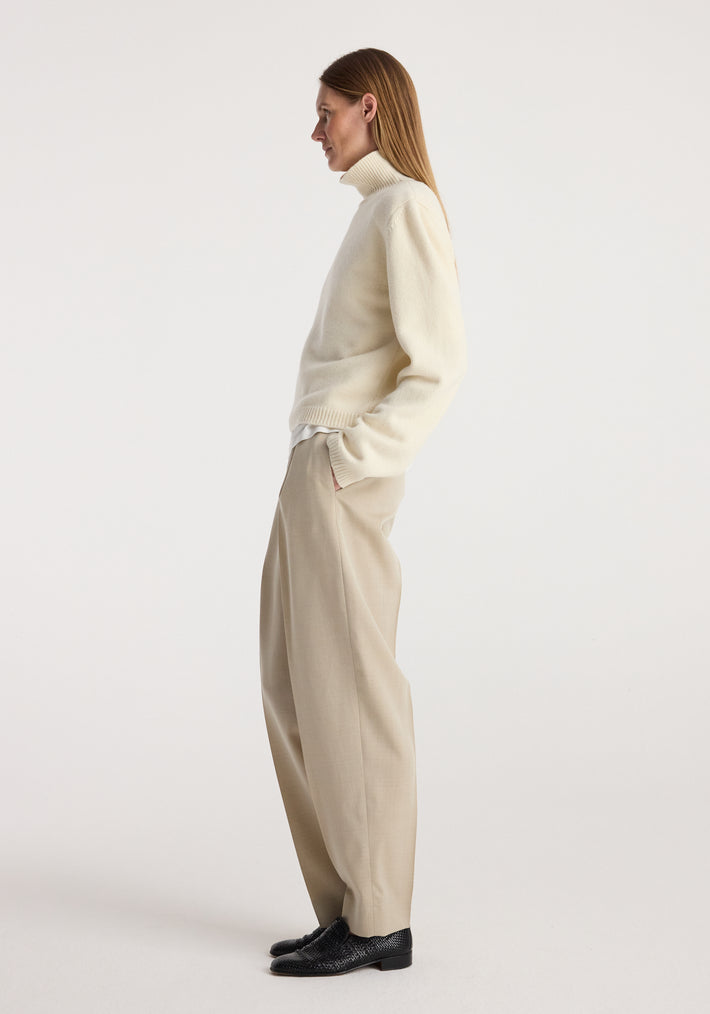 Woman wearing cream Statement shoulder cropped turtleneck | cream paired with beige wide-leg trousers and black shoes, standing sideways against a plain background.