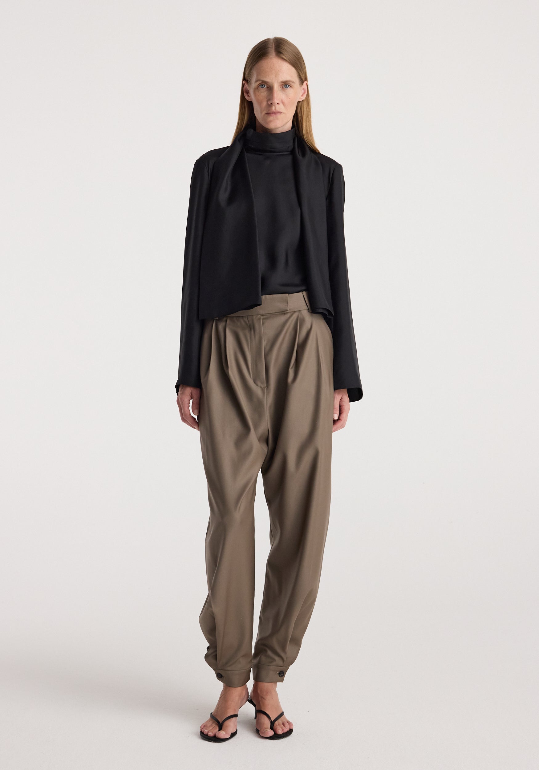 Woman wearing tailored cuff trousers | desert brown with a high-waisted fit, pleated front, and cuffs at the ankles paired with a black blouse and blazer.