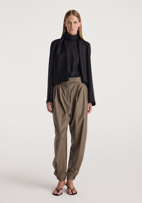 Woman wearing tailored cuff trousers | desert brown with a high-waisted fit, pleated front, and cuffs at the ankles paired with a black blouse and blazer.
