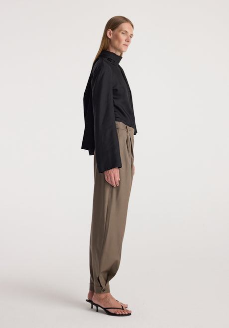 Woman wearing tailored cuff trousers | desert brown with a high-waisted fit, pleated front, and cuffs at the ankles paired with a black blouse and blazer.