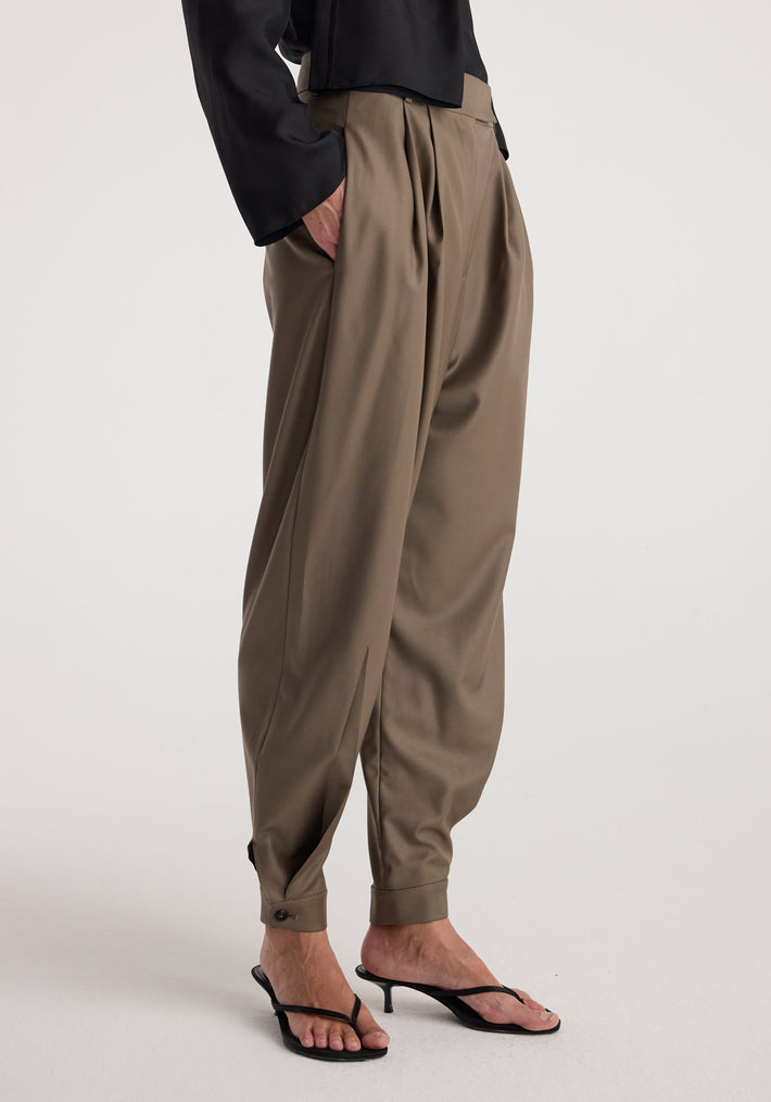 Person wearing tailored cuff trousers | desert brown with a loose fit and pleated front, styled with black heeled sandals and a black top.