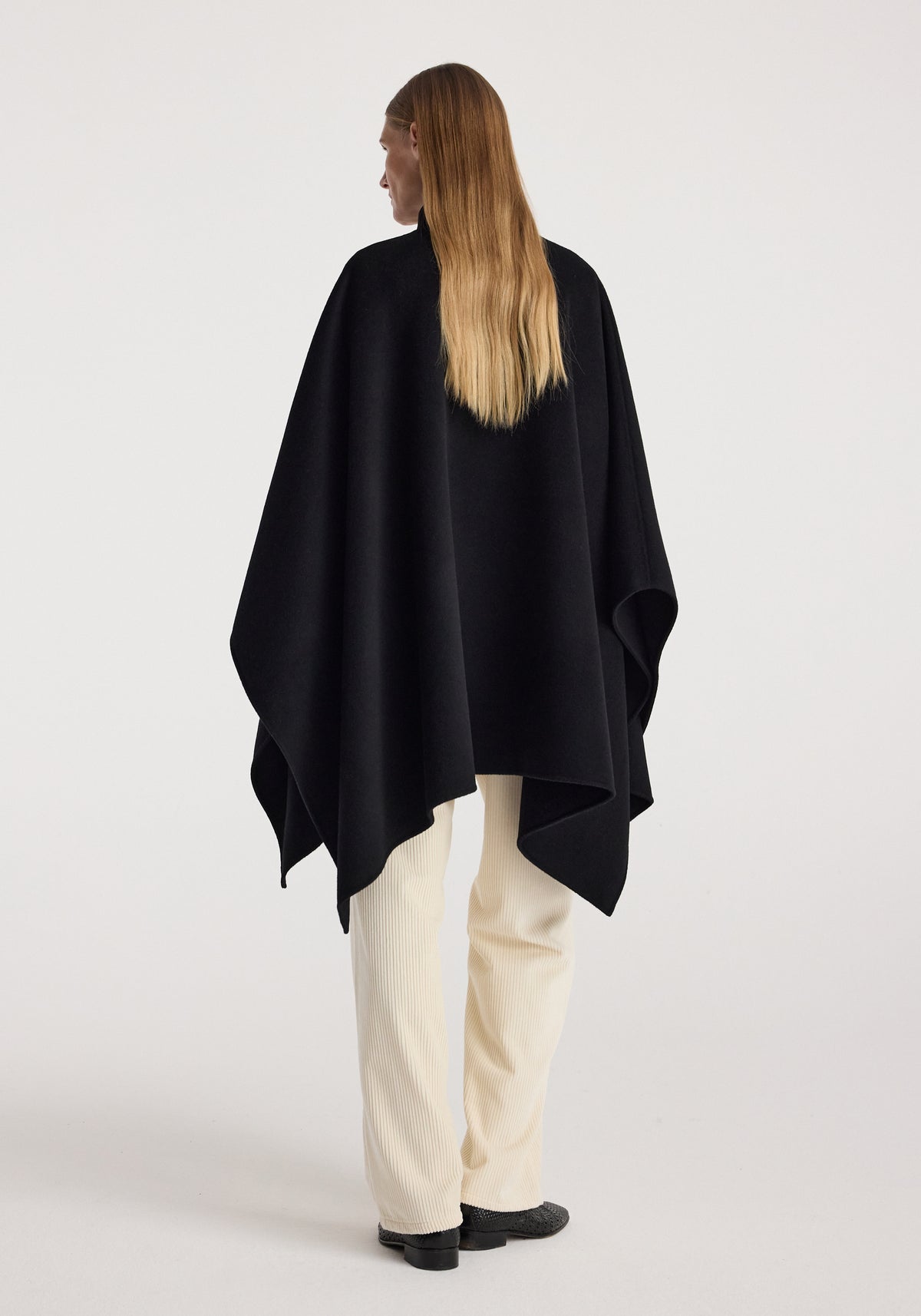 Woman seen from behind wearing a black Double-faced pankou poncho | black, paired with light-colored pants and black shoes against a plain background.