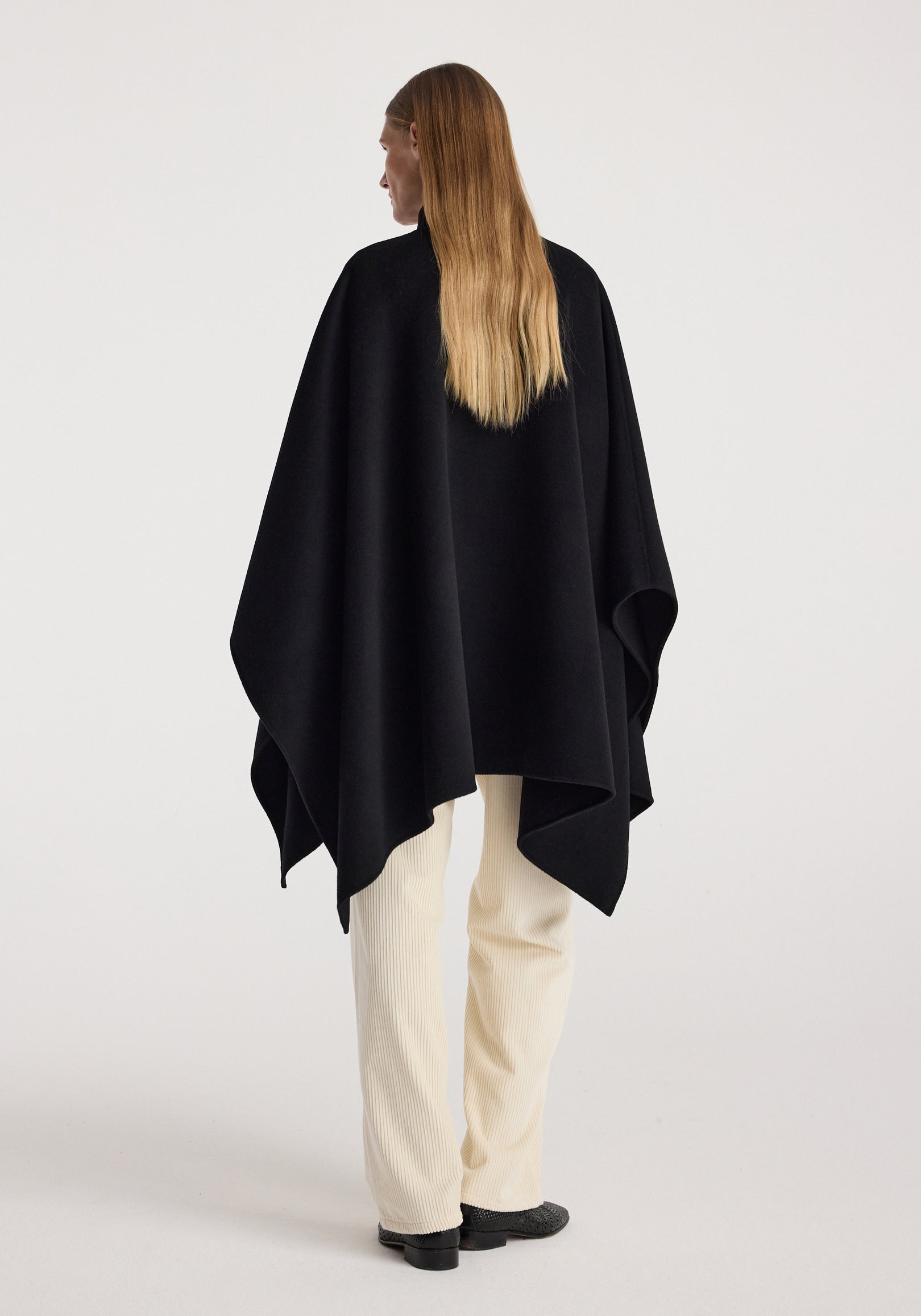 Woman seen from behind wearing a black Double-faced pankou poncho | black, paired with light-colored pants and black shoes against a plain background.