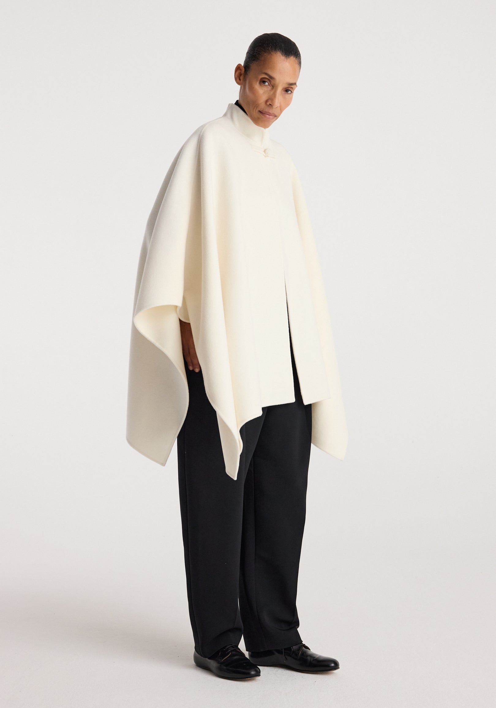 Woman wearing a flowing off white Double-faced pankou poncho | off white paired with black wide-leg trousers and black shoes, standing against a plain background.