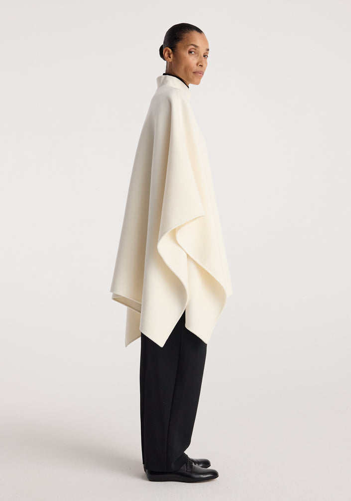 Woman wearing a flowing off white Double-faced pankou poncho | off white paired with black wide-leg trousers and black shoes, standing against a plain background.
