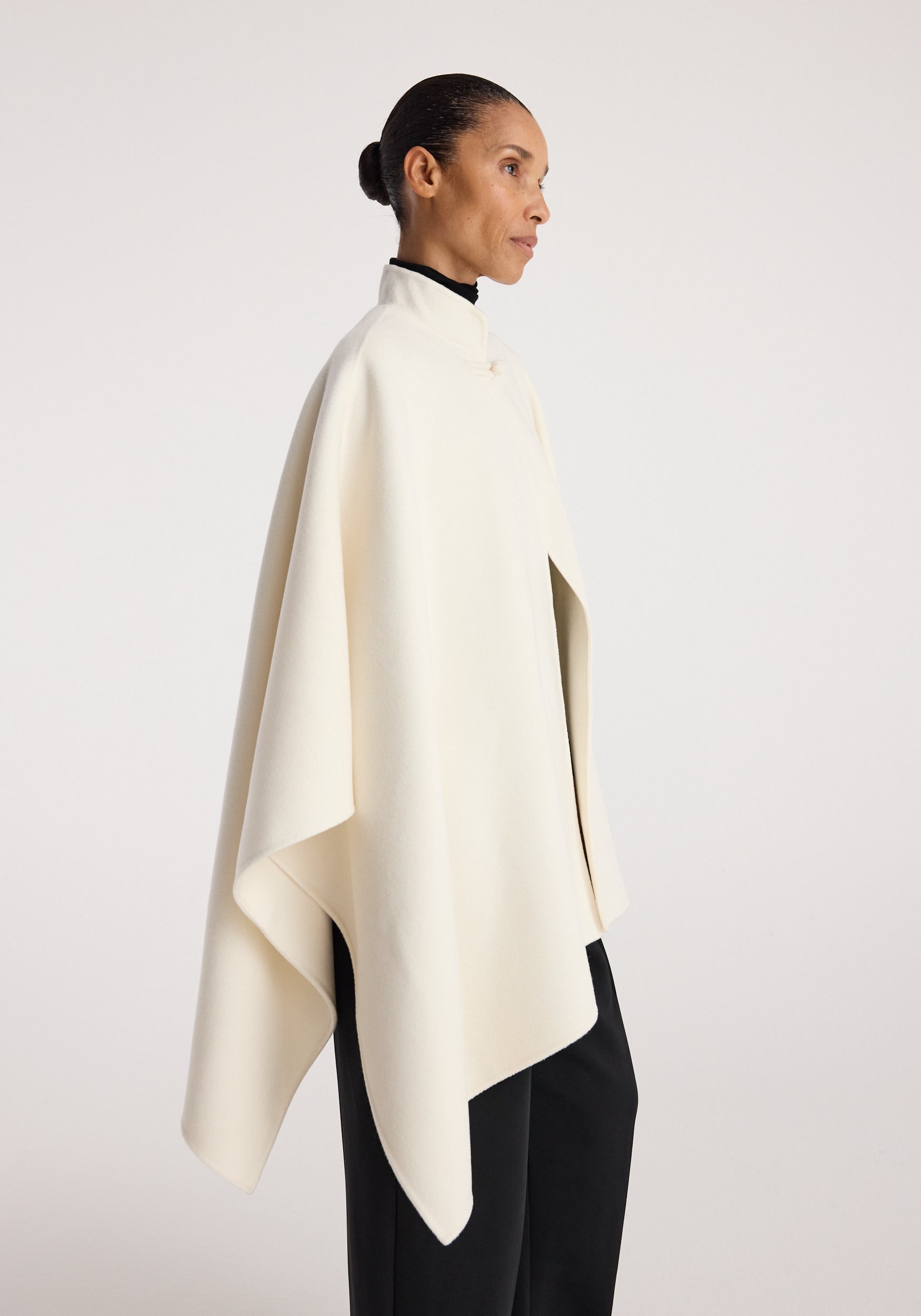 Woman wearing an elegant double-faced pankou poncho off white draped over black clothing against a plain background, showcasing the garment's clean lines and soft texture.
