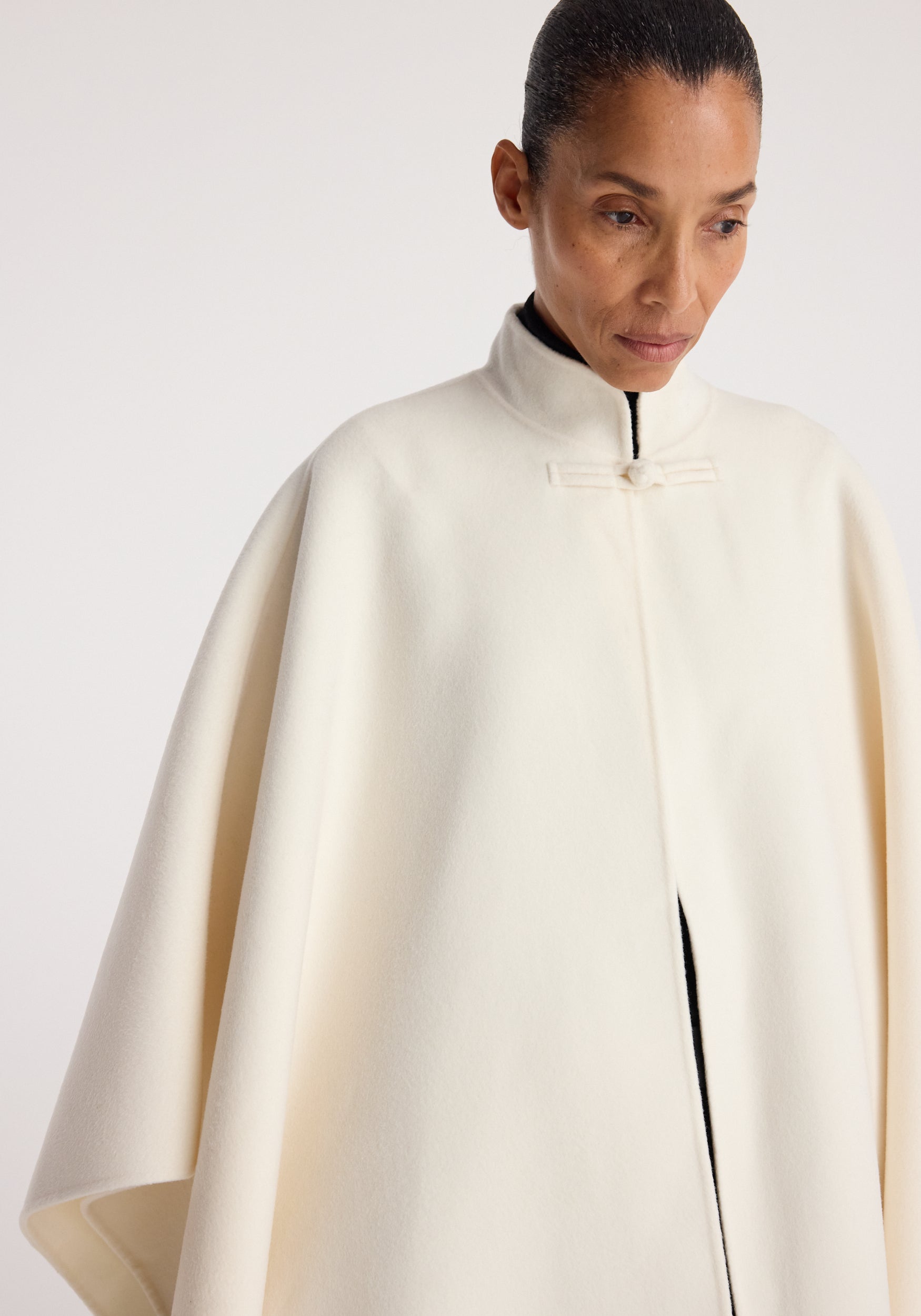 Woman wearing an off white, high-collar, elegant Double-faced pankou poncho | off white with a simple fastening at the neck, draped over her shoulders against a plain background.