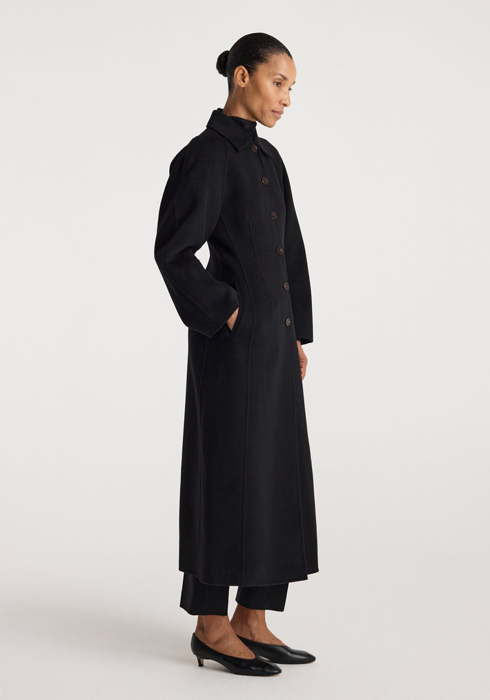 Woman wearing a minimalist, long black coat with buttons and side pockets, styled with black pants and low black heels, showcasing the Double-faced elongated sculptural coat | black.