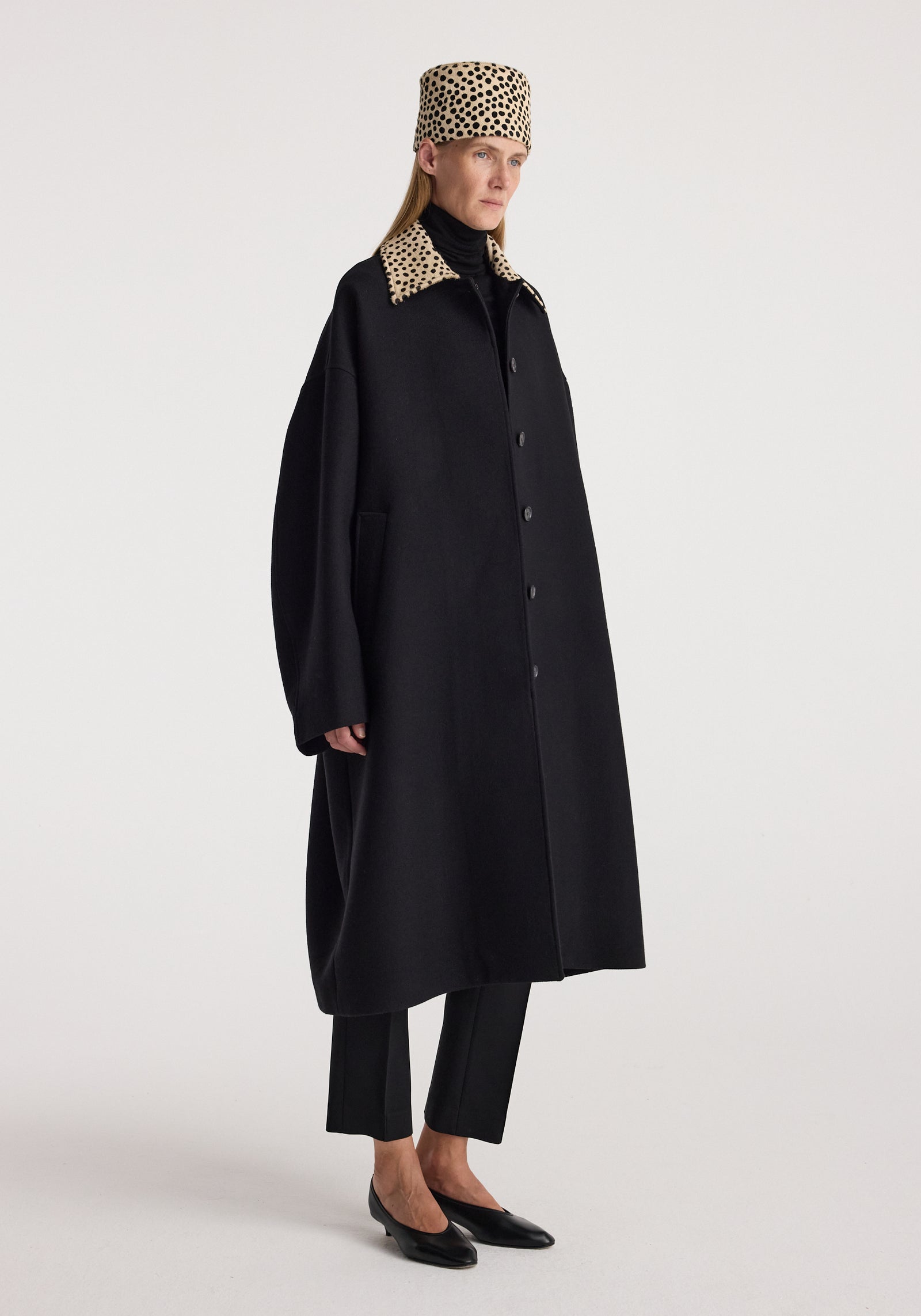 Model wearing a long black wool coat with a cheetah print collar and black buttons, paired with black pants and black shoes, styled with a matching cheetah print headscarf. The product is named Cheetah collar wool coat | black.