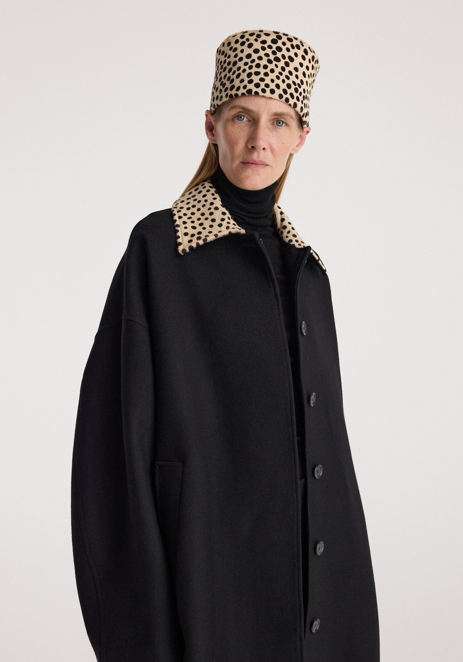 Woman wearing a black Cheetah collar wool coat | black with a leopard-print collar, styled with a matching spotted hat and a black turtleneck underneath.