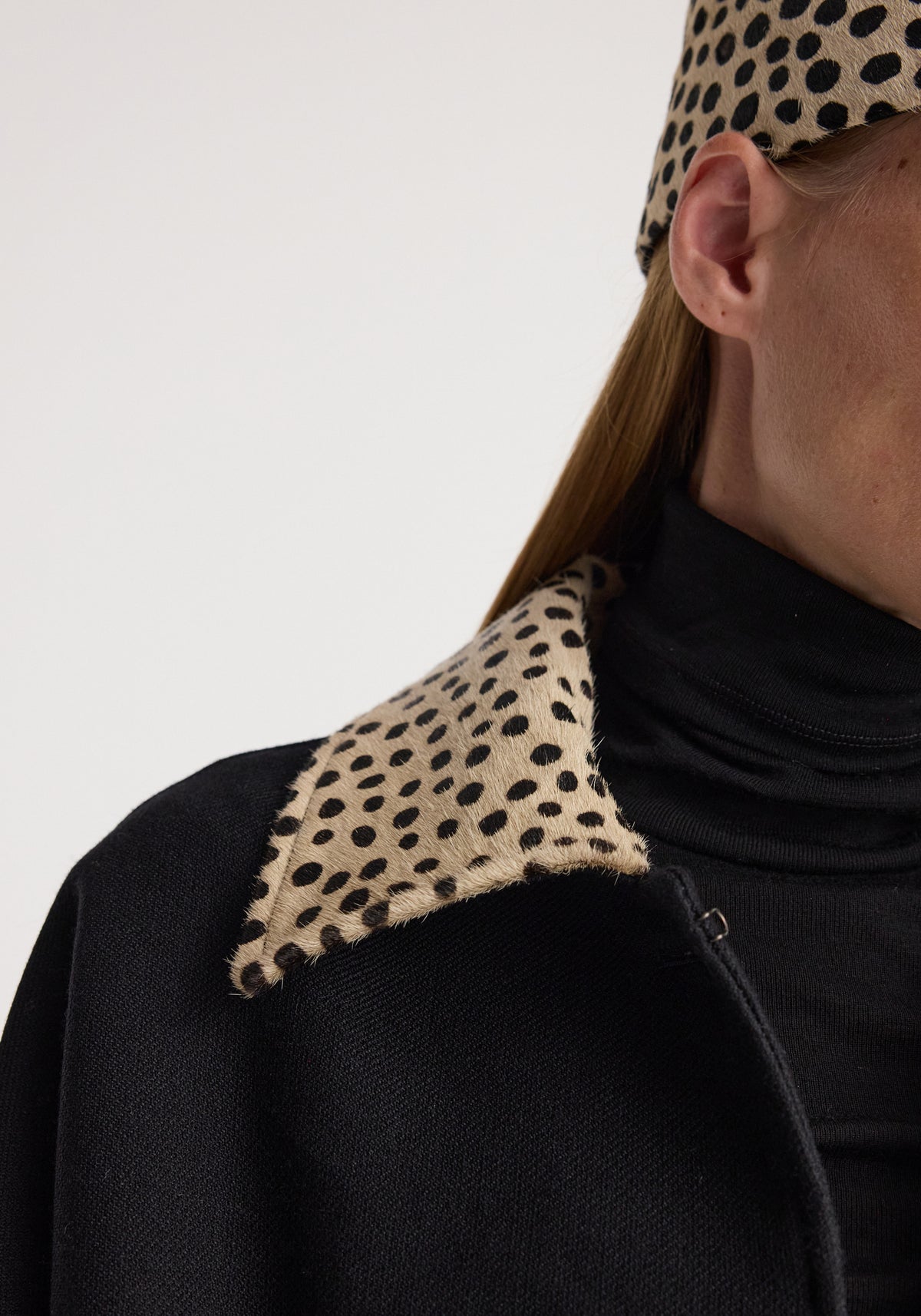Close-up of a black wool coat featuring a cheetah collar with a spotted pattern, worn over a black turtleneck, highlighting the texture and design of the cheetah collar wool coat | black.