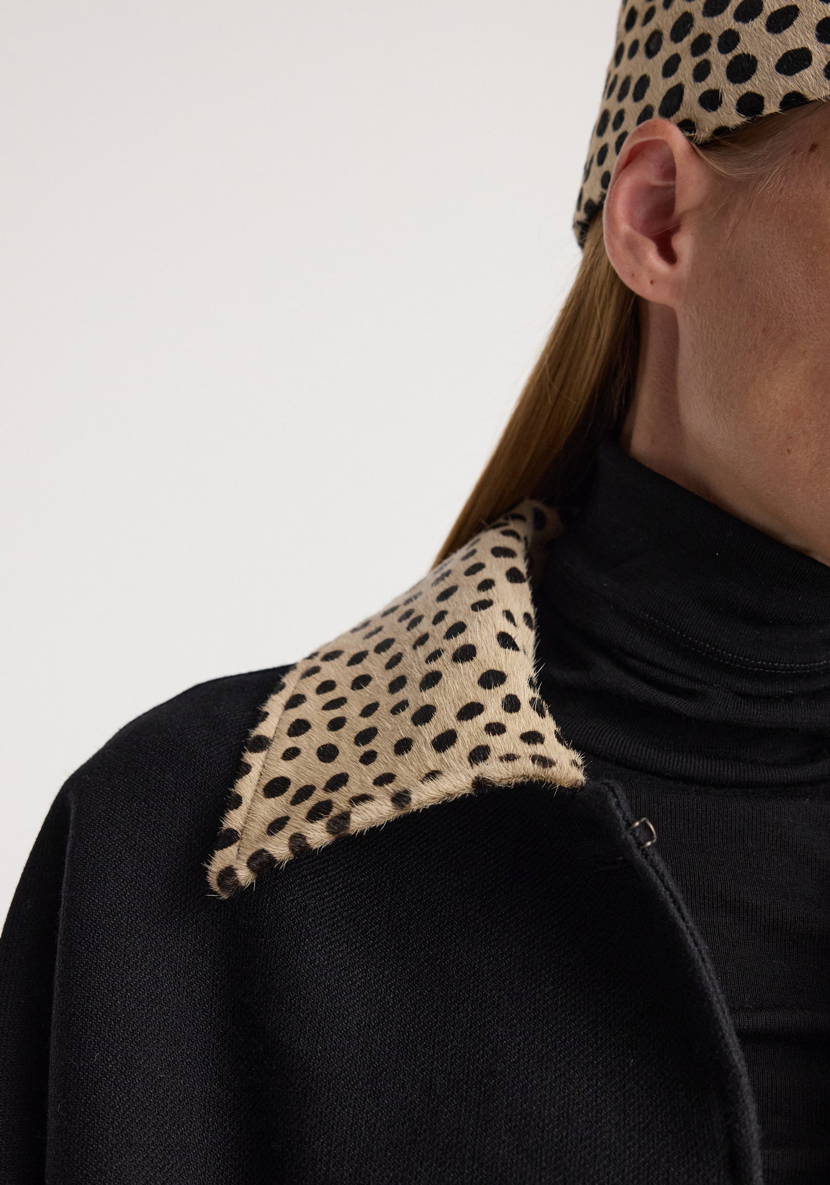 Close-up of a black wool coat featuring a cheetah collar with a spotted pattern, worn over a black turtleneck, highlighting the texture and design of the cheetah collar wool coat | black.