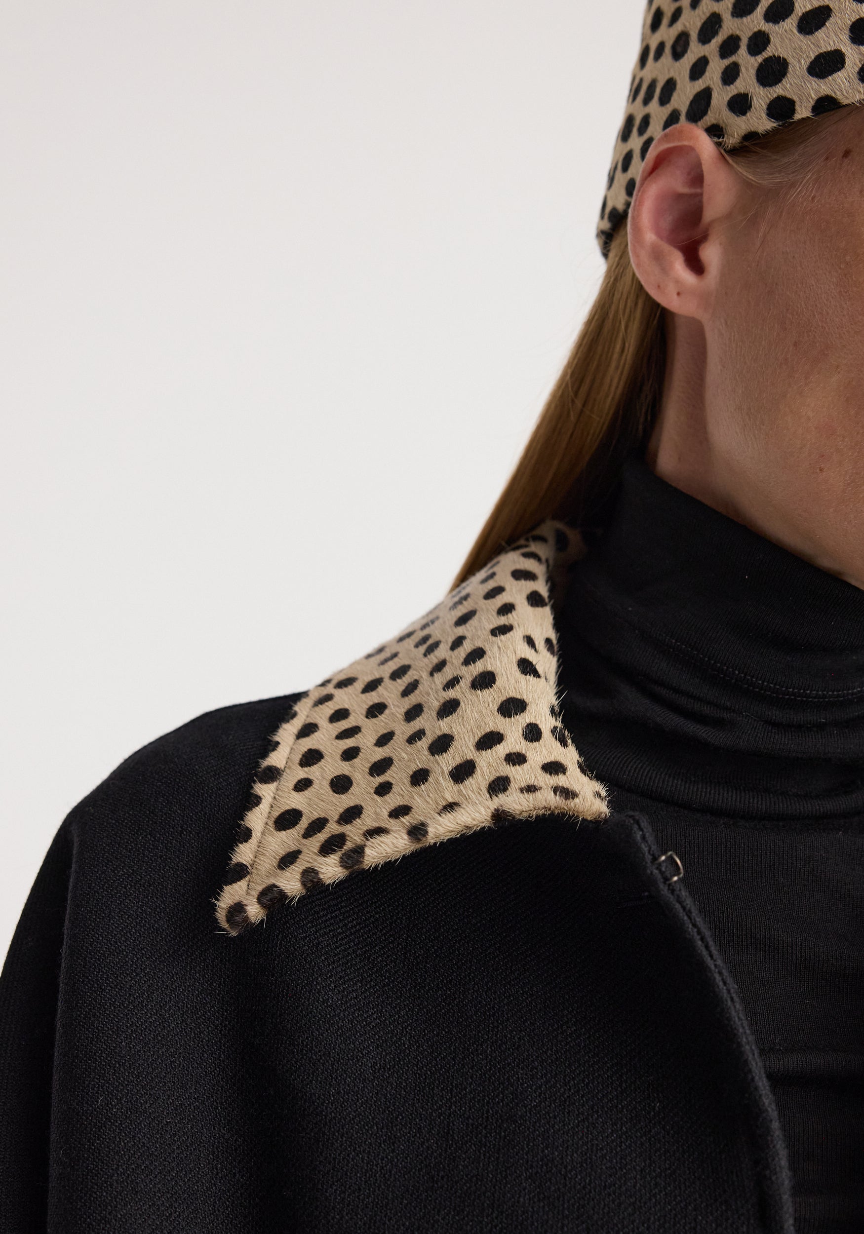 Close-up of a black wool coat featuring a cheetah collar with a spotted pattern, worn over a black turtleneck, highlighting the texture and design of the cheetah collar wool coat | black.