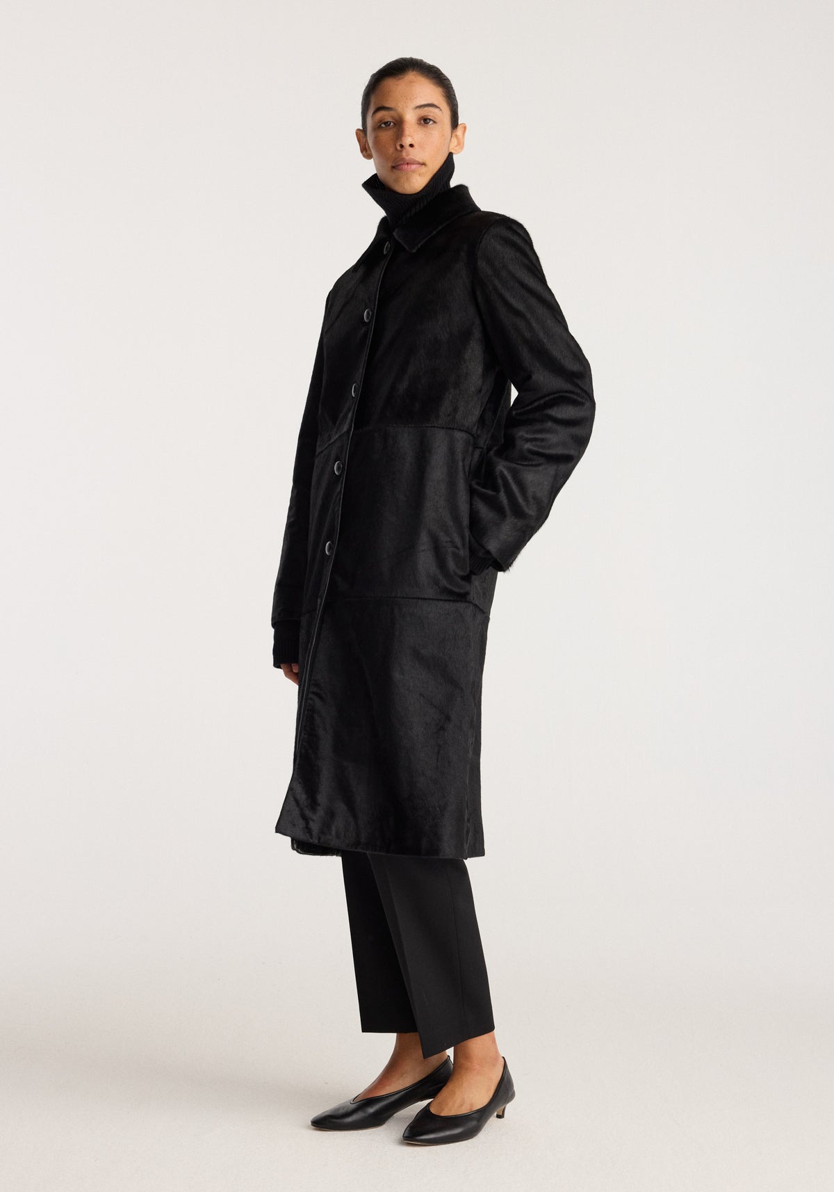 Black ponyhair coat | black worn by a model with a high collar button front long sleeves side pockets and a below knee length silhouette.