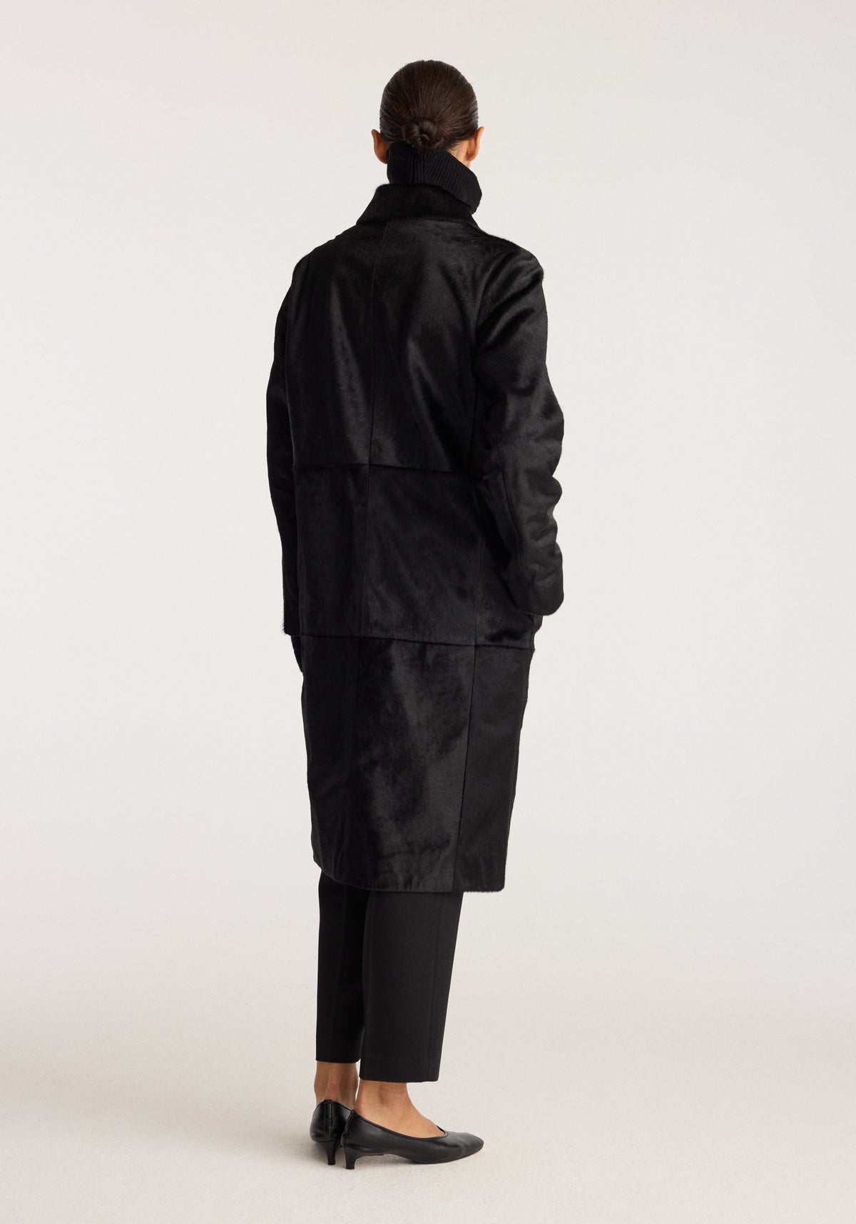 Black ponyhair coat | black shown from the back on a model with a high collar and mid-length silhouette