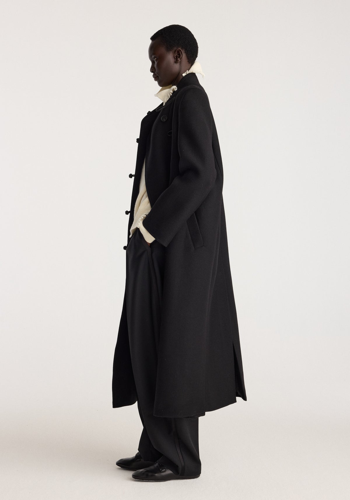 Pankou closure wool coat | black shown in side profile on a model with long silhouette, toggle closures, wide lapels, and matching dark trousers