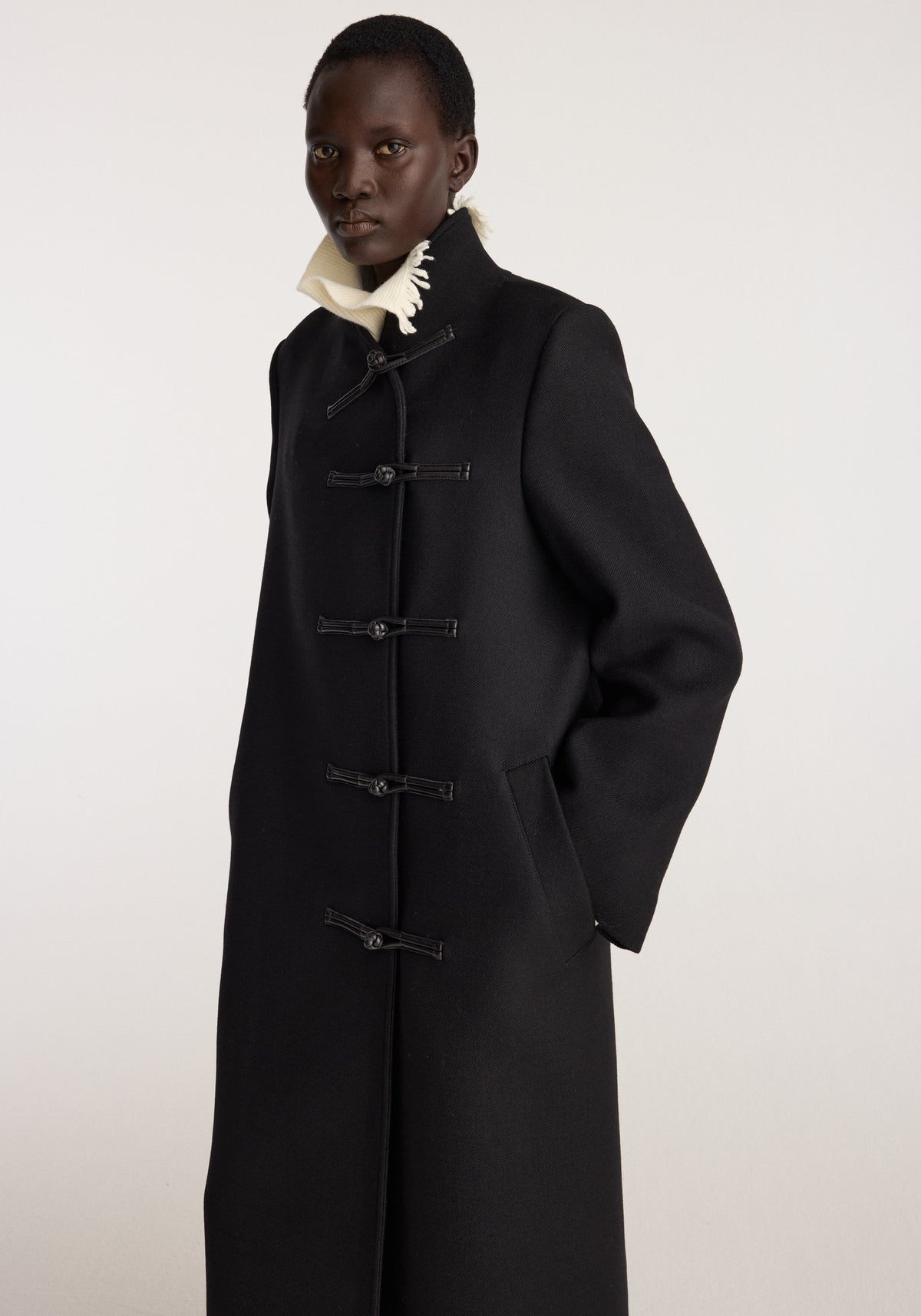 Pankou closure wool coat | black worn by a model featuring a high collar horn closures long sleeves and a tailored full length silhouette