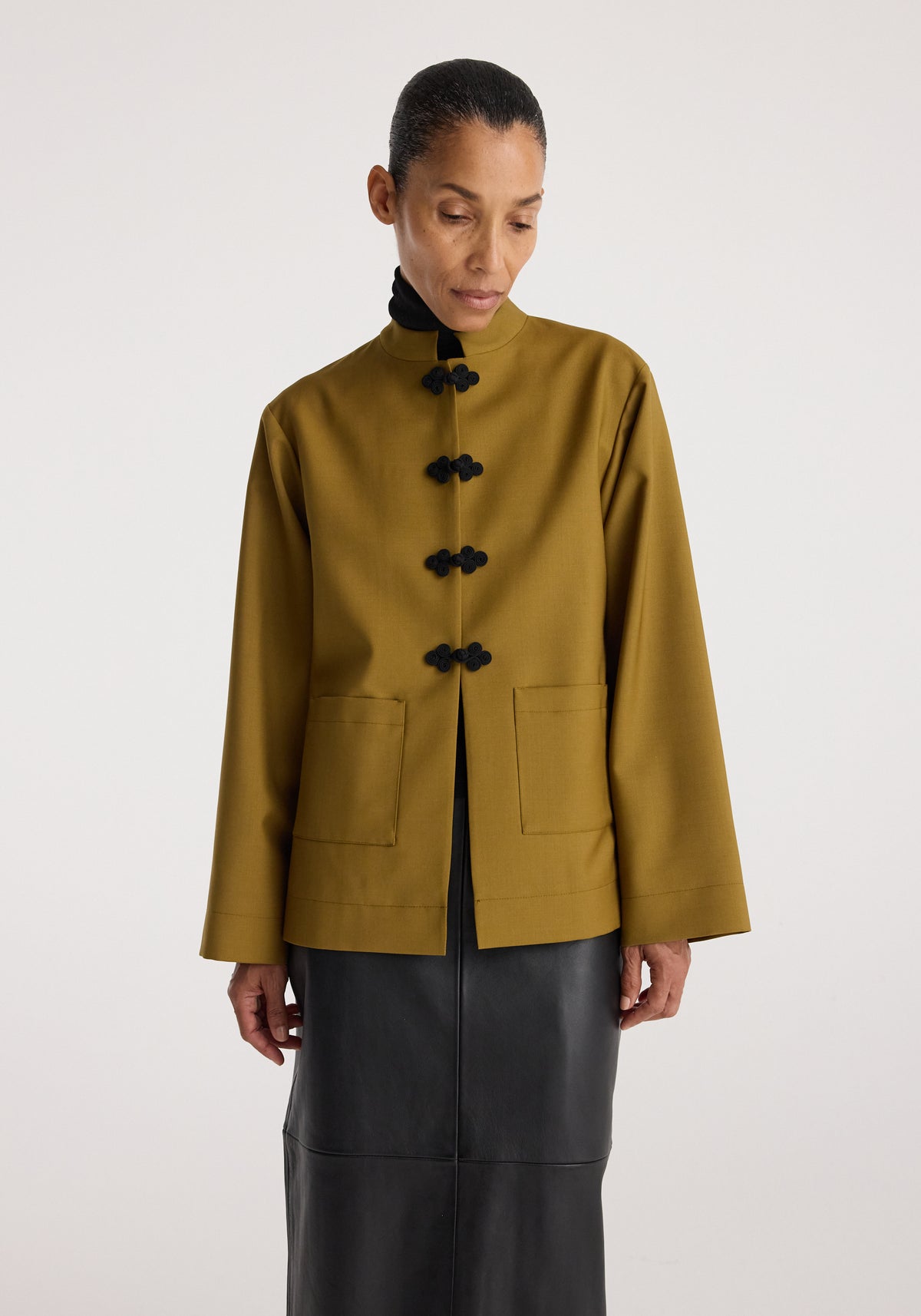 Woman wearing a mustard long-sleeve jacket with black pankou closures and front pockets, styled with a black turtleneck and a black skirt, Pankou closure jacket | mustard.