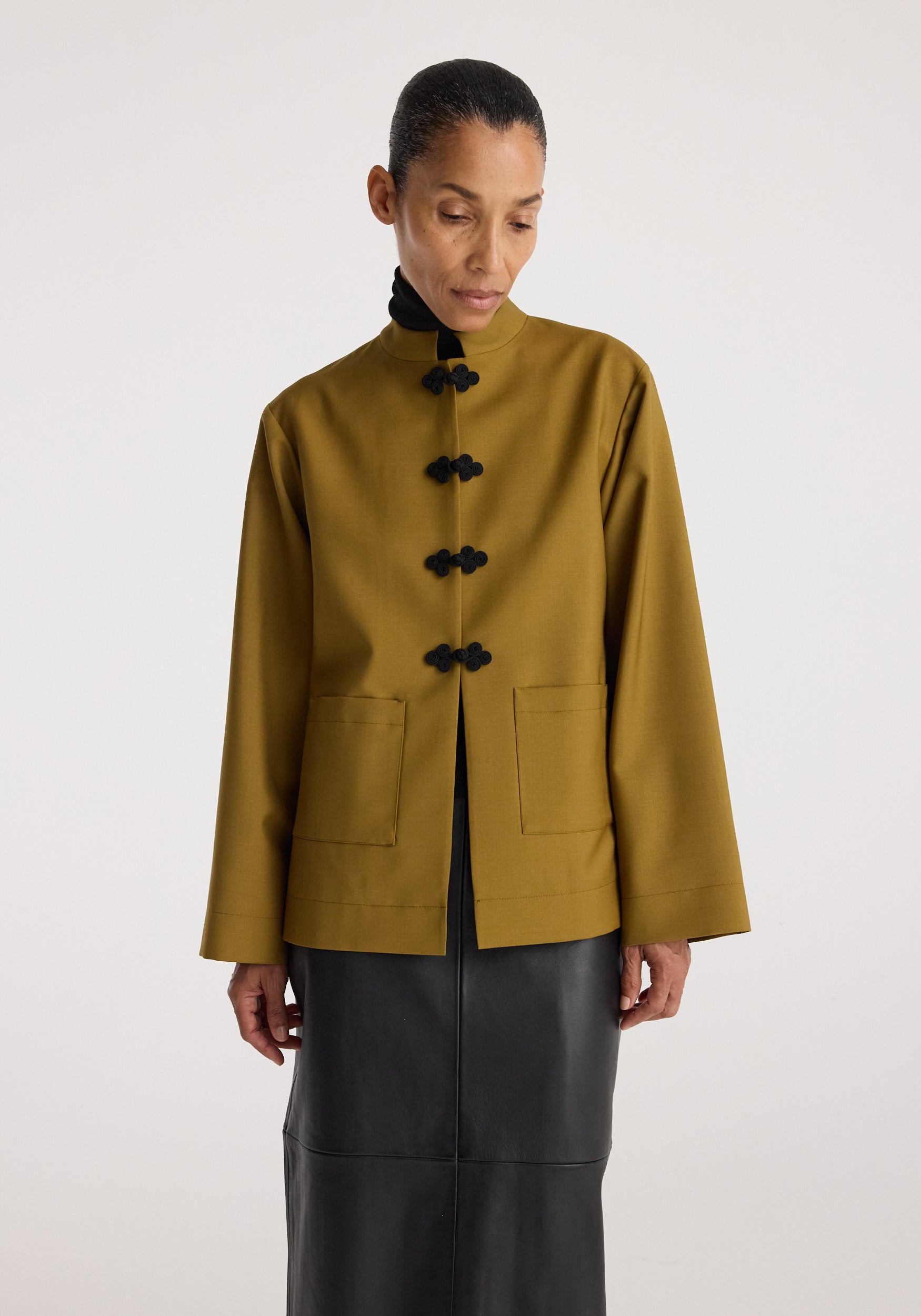 Woman wearing a mustard long-sleeve jacket with black pankou closures and front pockets, styled with a black turtleneck and a black skirt, Pankou closure jacket | mustard.