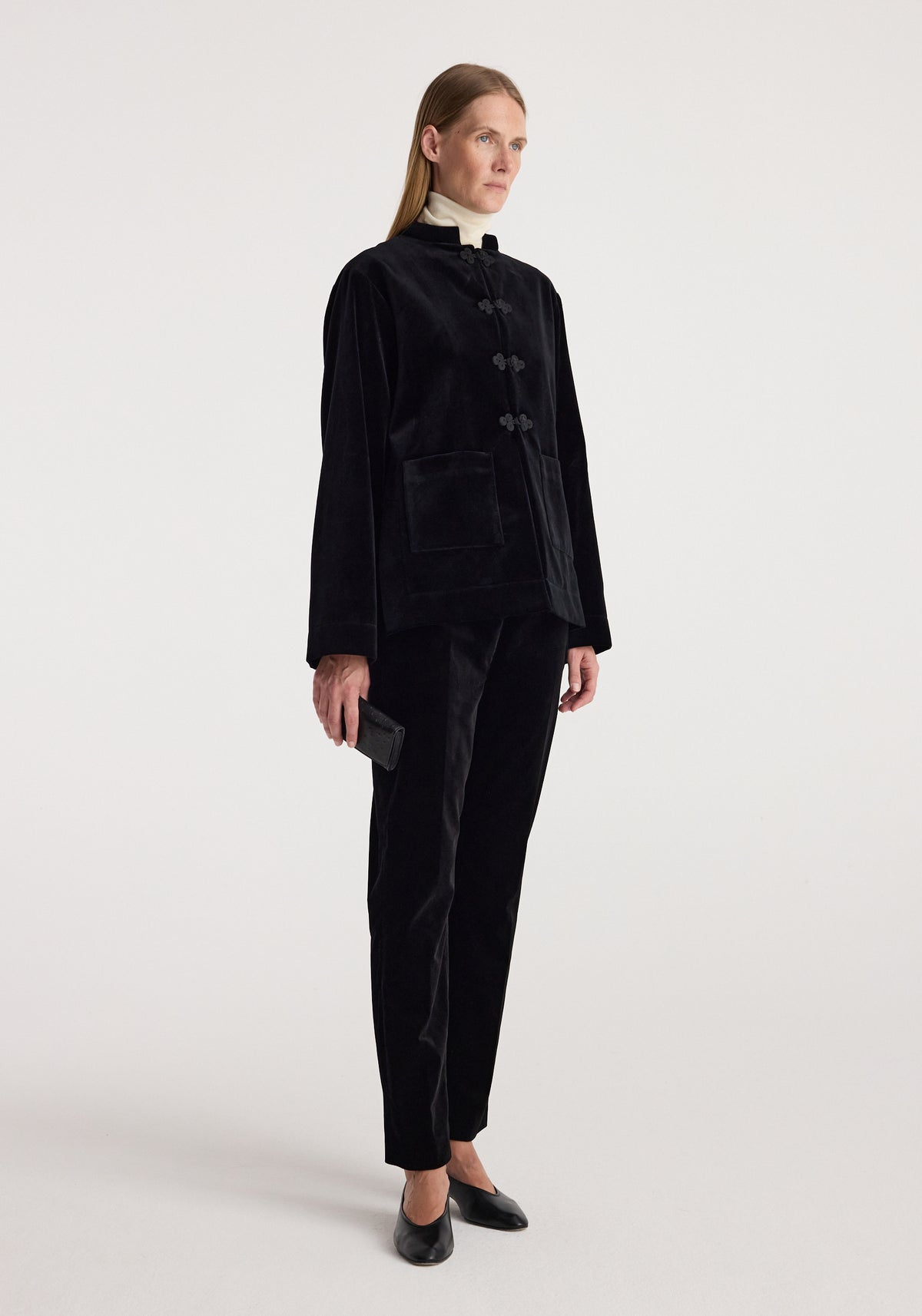 Woman wearing a Pankou closure velvet jacket | black with front pockets, paired with matching black velvet pants, standing against a plain white background.