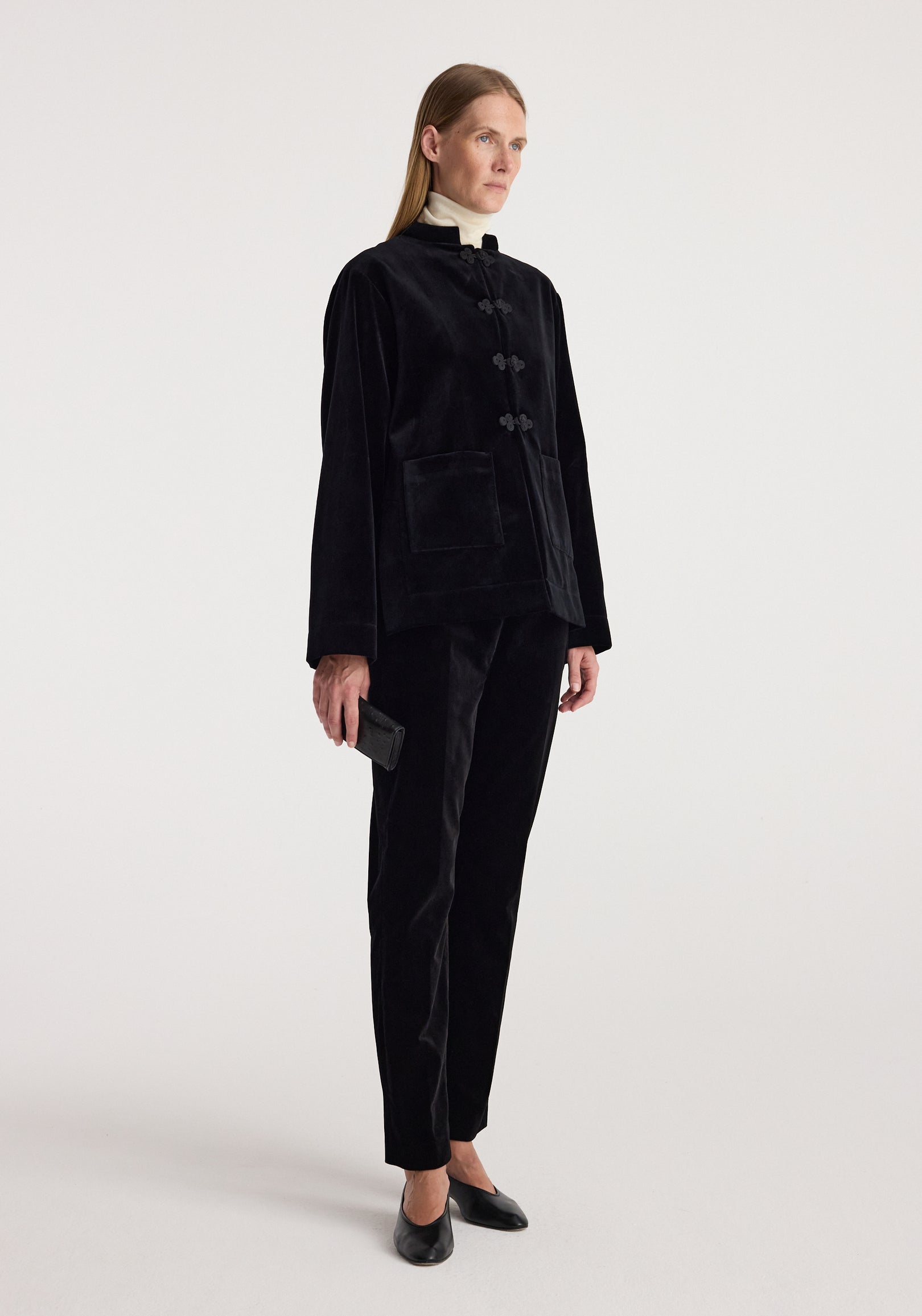 Woman wearing a Pankou closure velvet jacket | black with front pockets, paired with matching black velvet pants, standing against a plain white background.