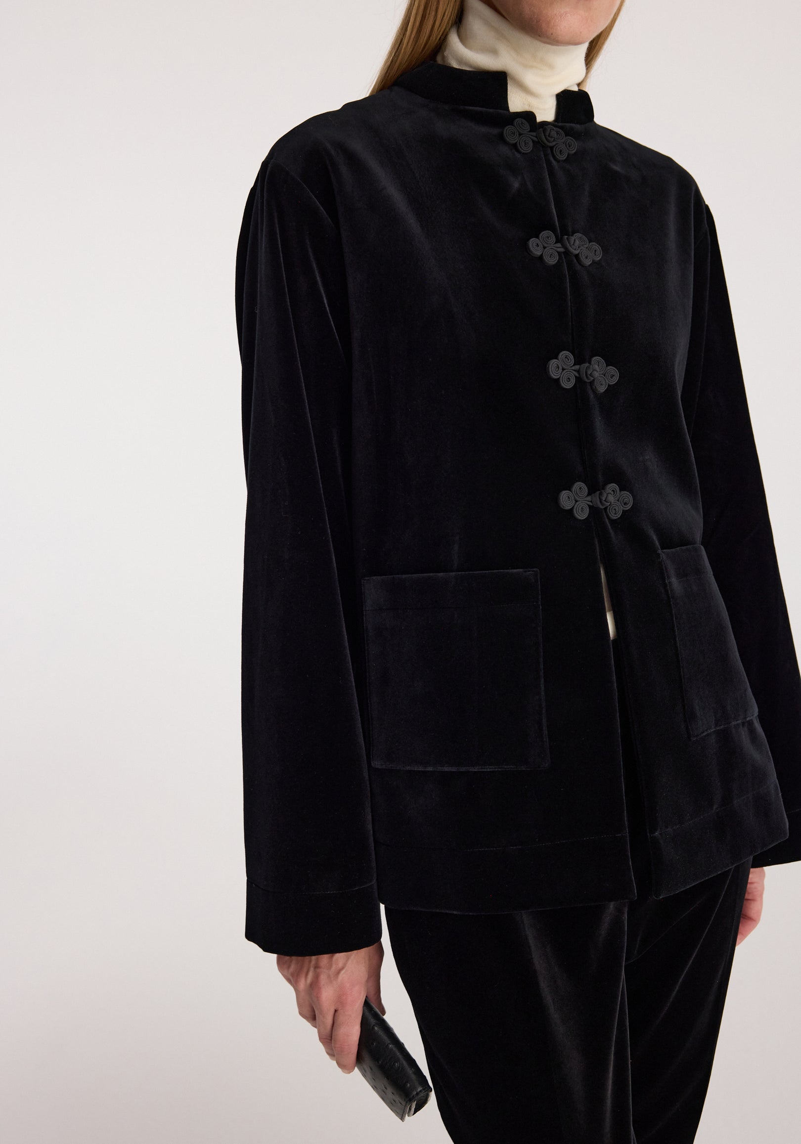 Black velvet jacket with Pankou closure details, featuring a stand collar, long sleeves, and front patch pockets, styled over a light turtleneck sweater.