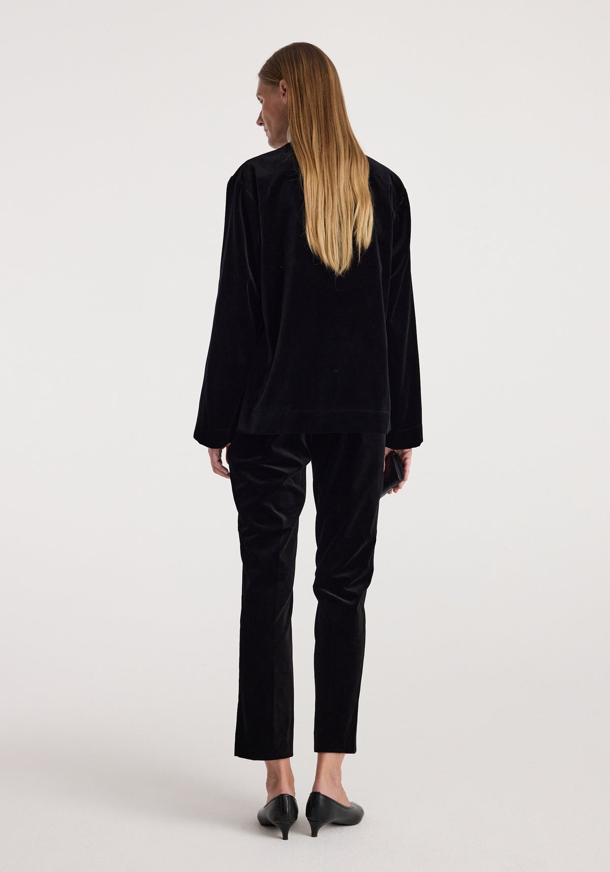 Woman wearing a black Pankou closure velvet jacket | black, shown from the back, paired with matching black velvet pants and black heeled shoes.